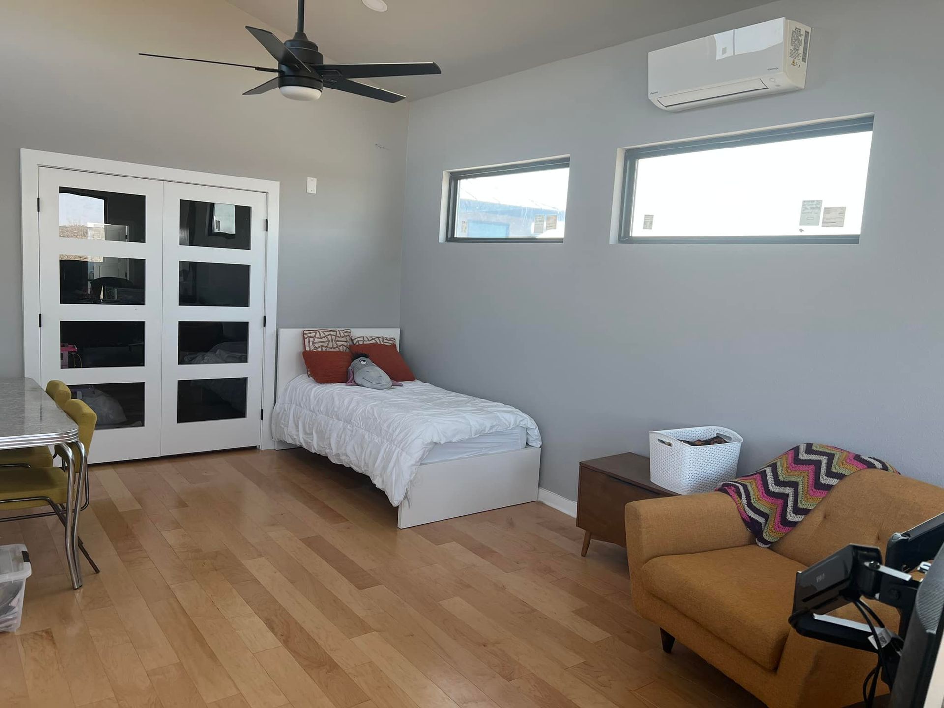 Modern bedroom with white bed, tan sofa, wood floor, and black ceiling fan.