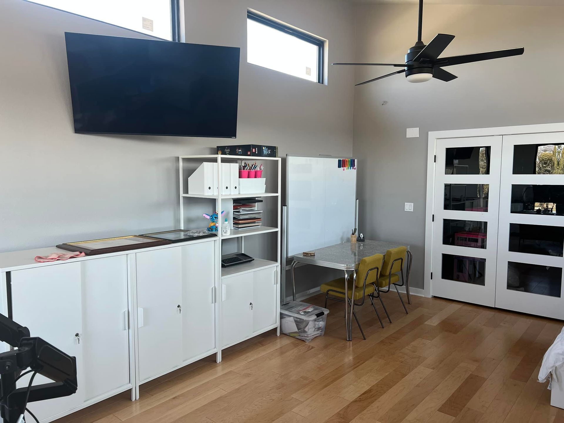 Modern living room with wall-mounted TV, white cabinets, fridge, desk, and glass-front storage cabinets