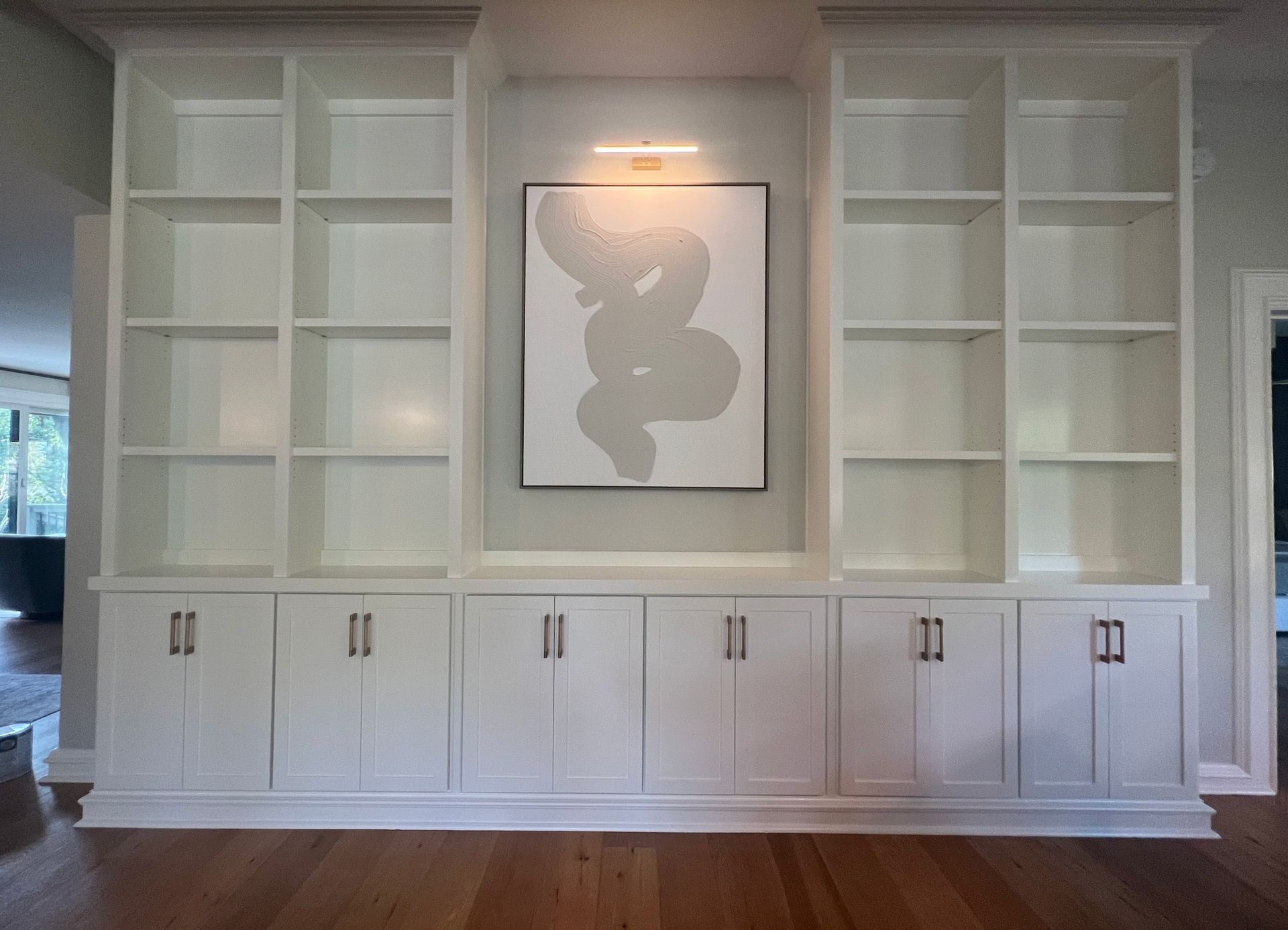 Built-in white shelving and cabinets framing a central abstract artwork in a bright room