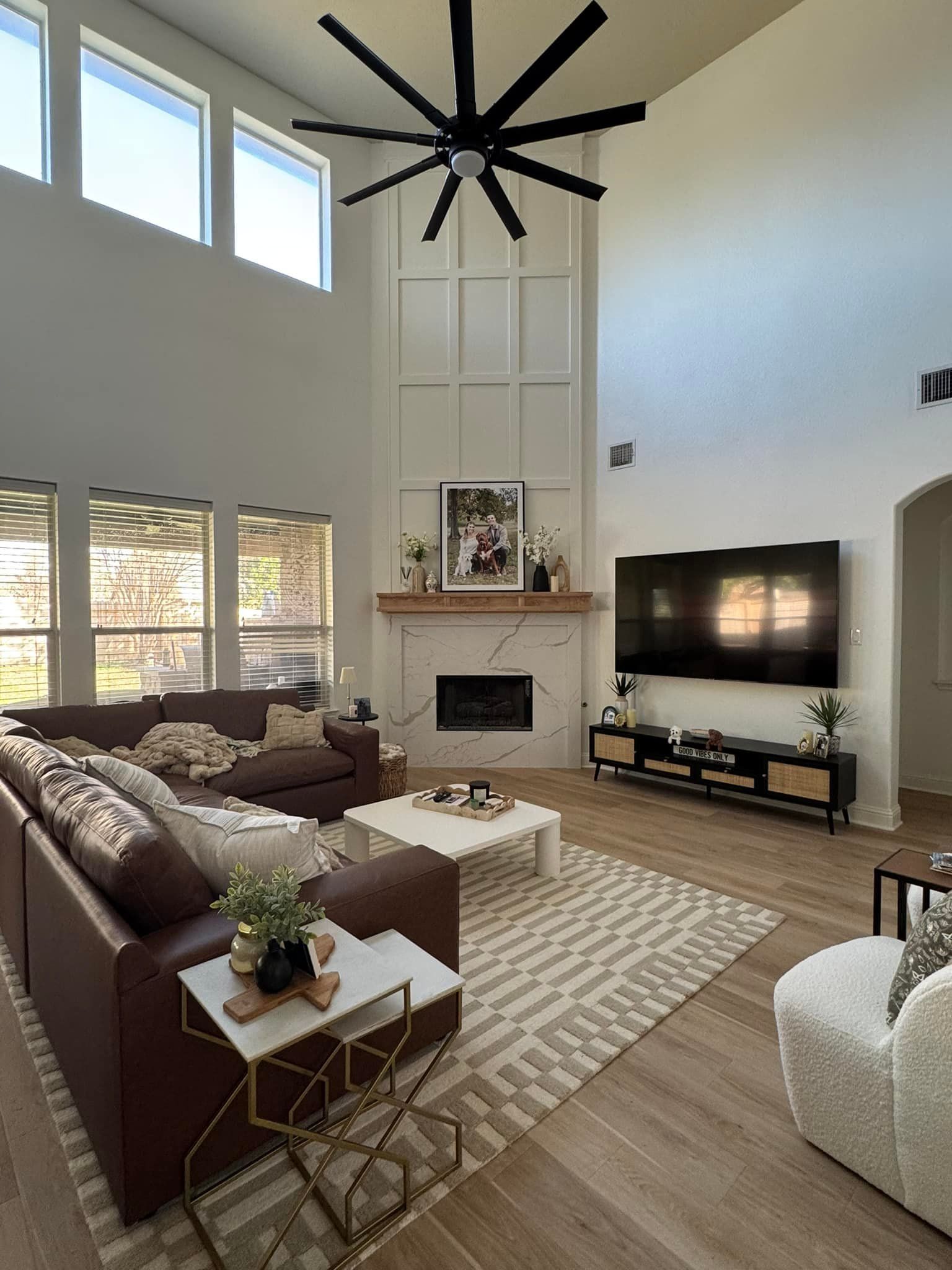 Modern living room with high ceilings, fireplace, large TV, brown sectional, and neutral decor