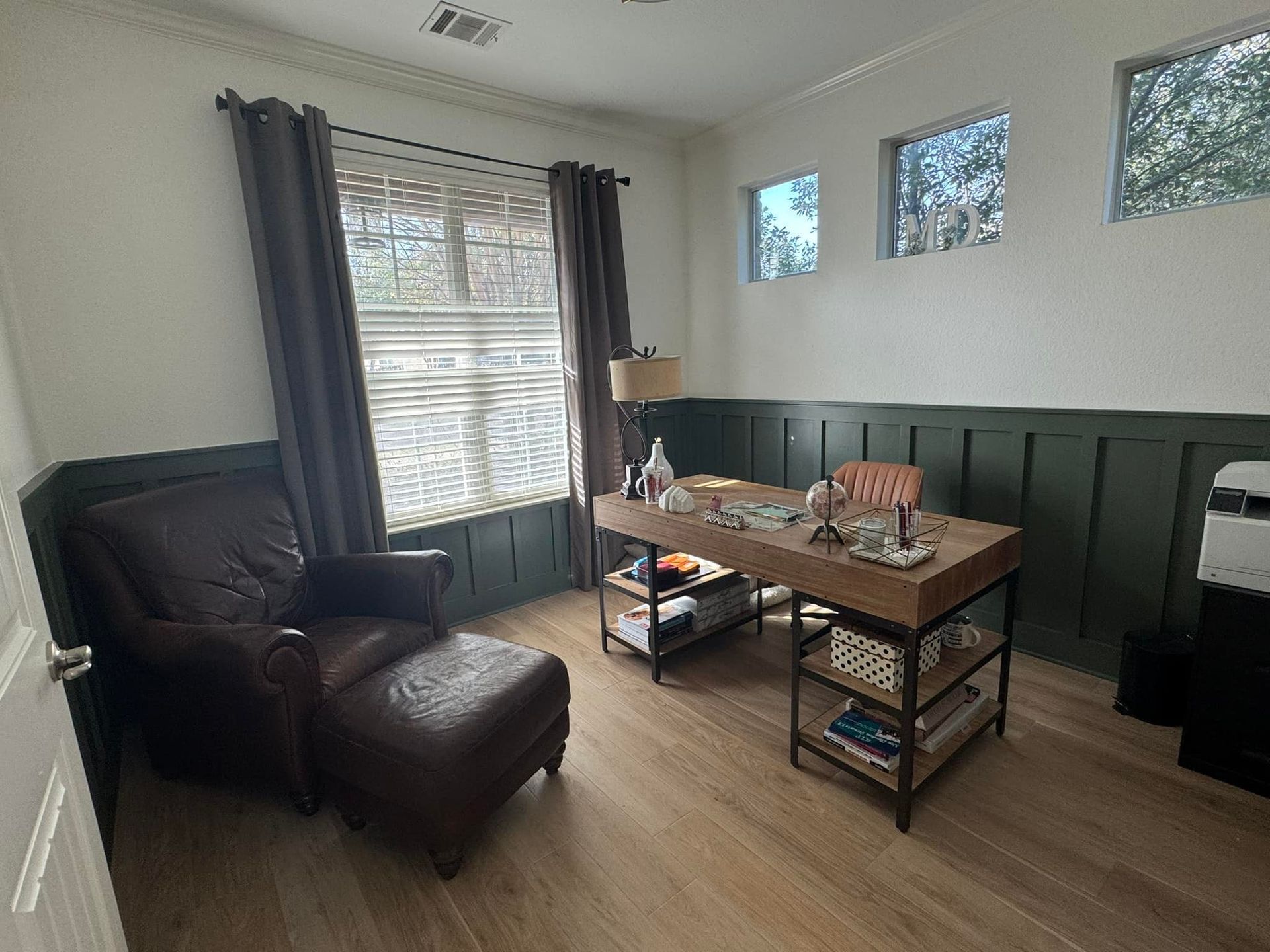 Cozy living room with a leather chair, wooden table, window curtains, and dark green wall paneling