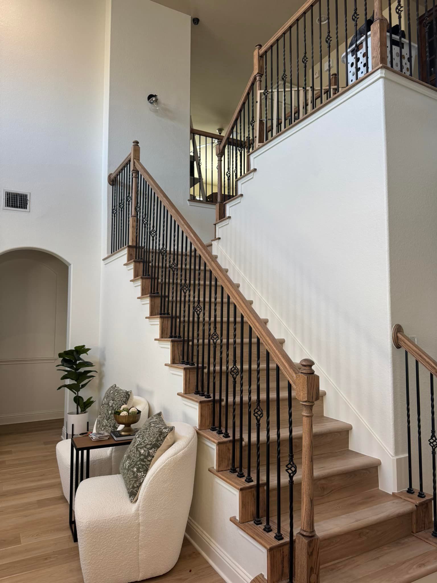 Staircase with dark iron railing and wood steps in a bright entryway beside a white chair and potted plant