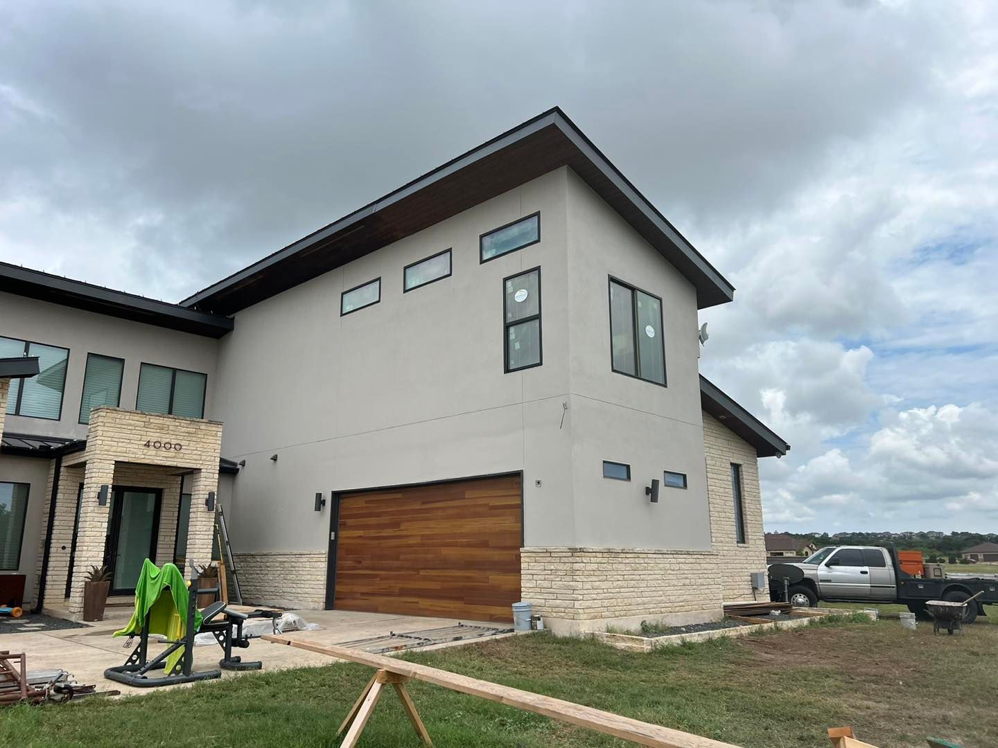 Modern two-story house with stone trim, wood garage door, and a worker in the front yard