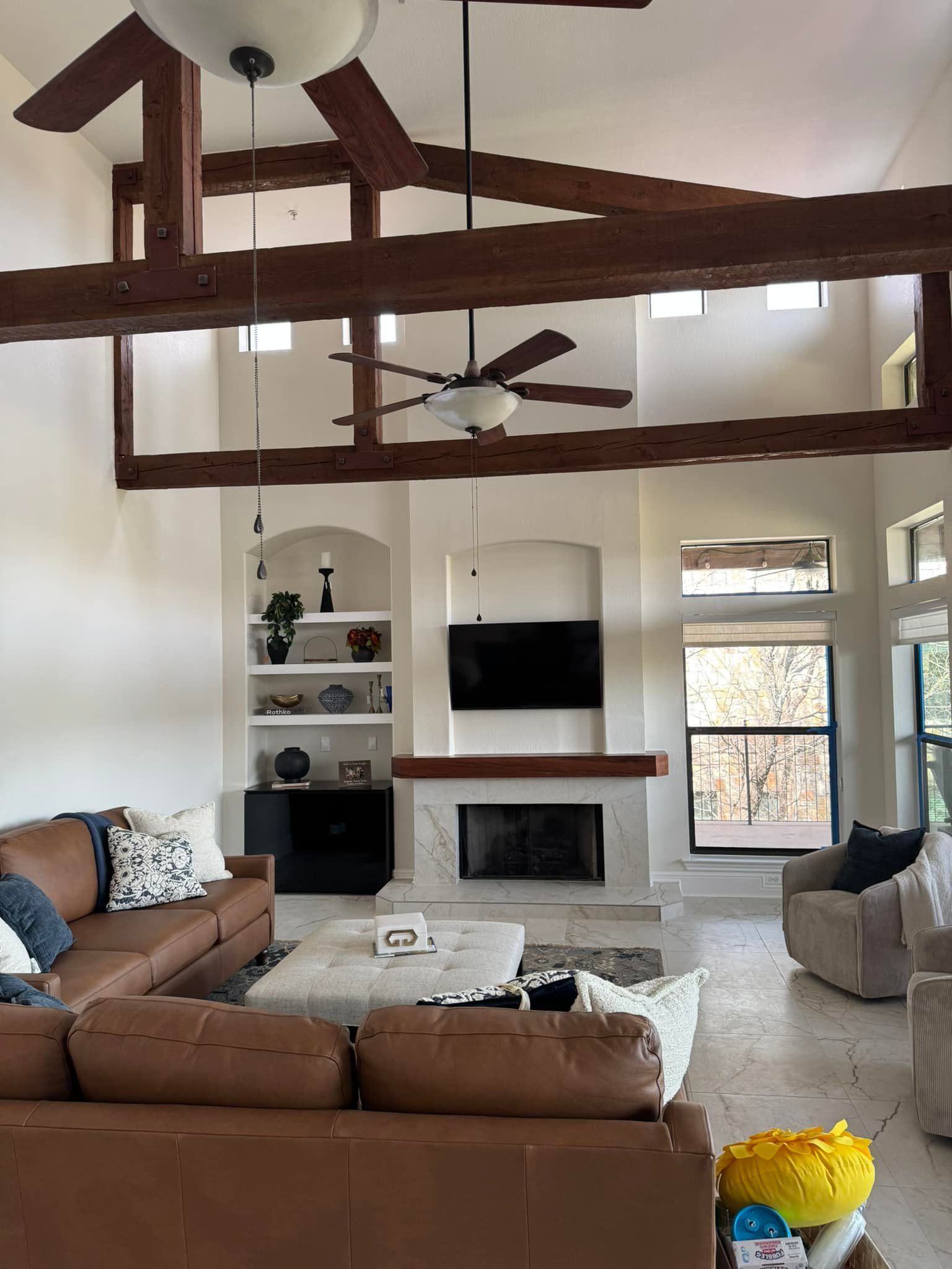 Bright living room with wood beams, fireplace, TV, and brown sectional sofa under vaulted ceiling.