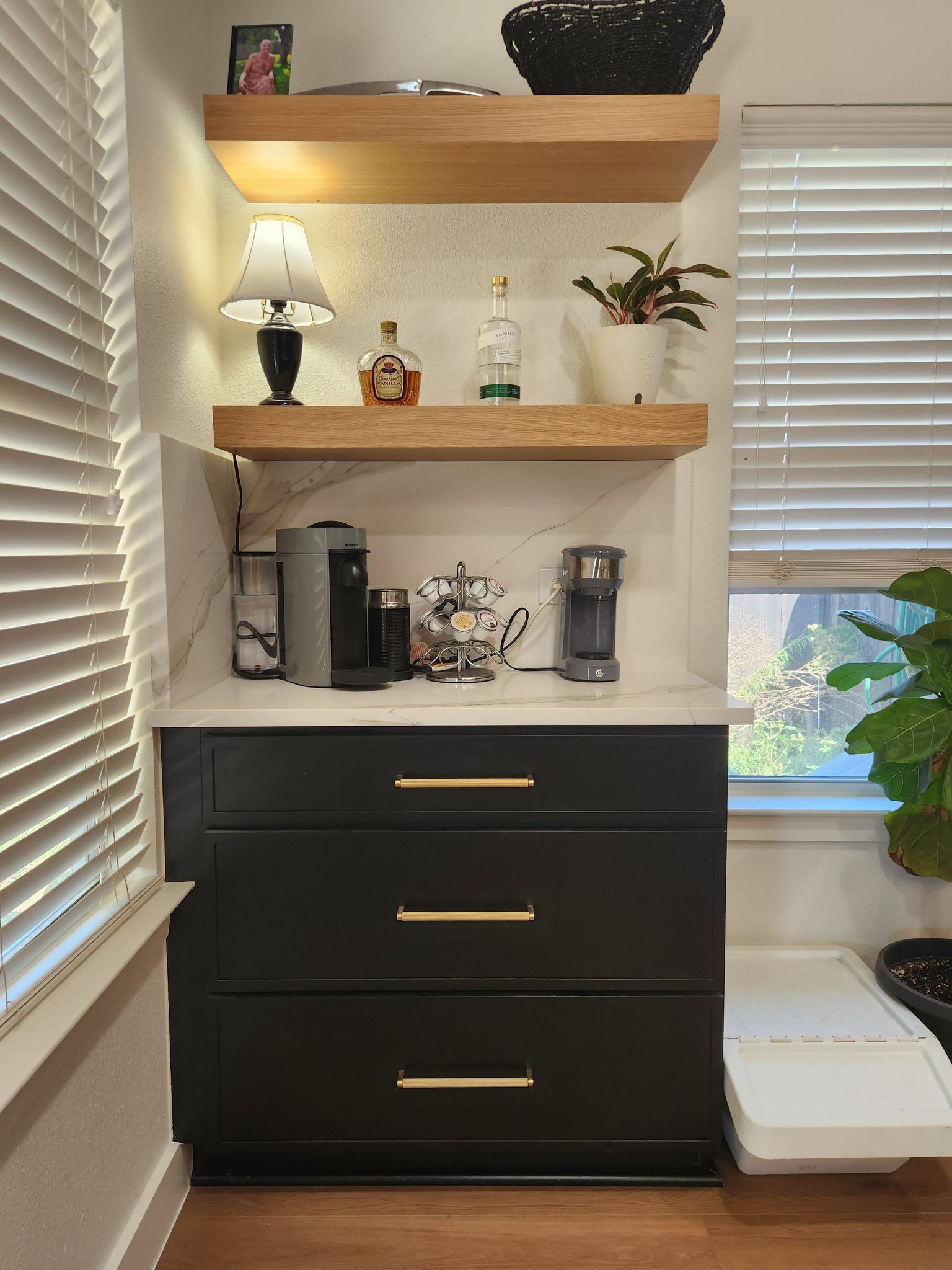 Built-in nook with floating wood shelves, black drawers, and coffee station beside a window with blinds.