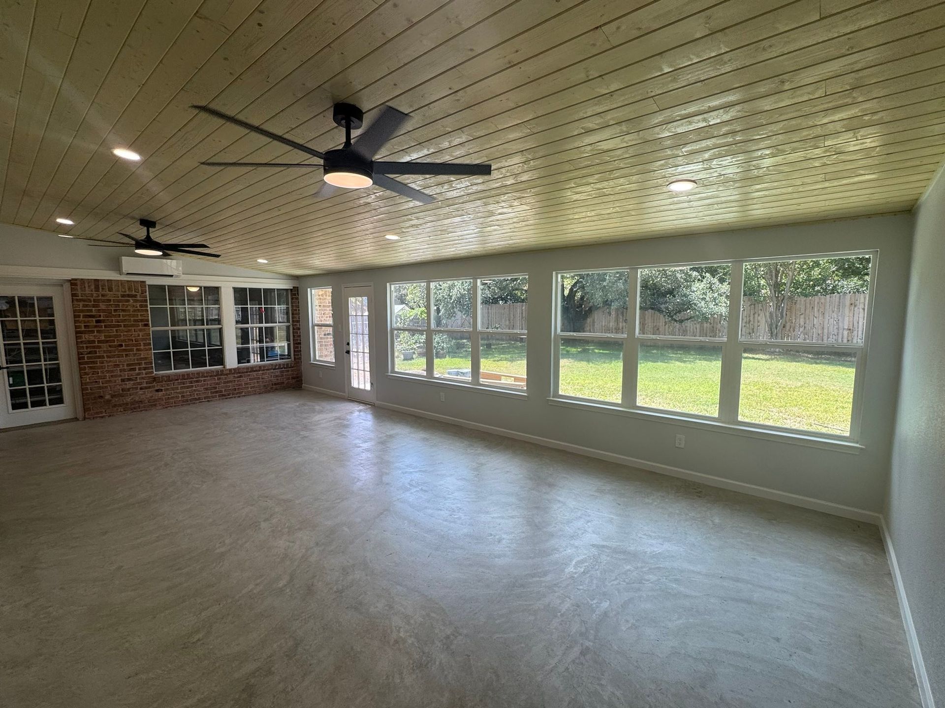 Enclosed sunroom with ceiling fans, large windows, and tiled floor overlooking a green yard