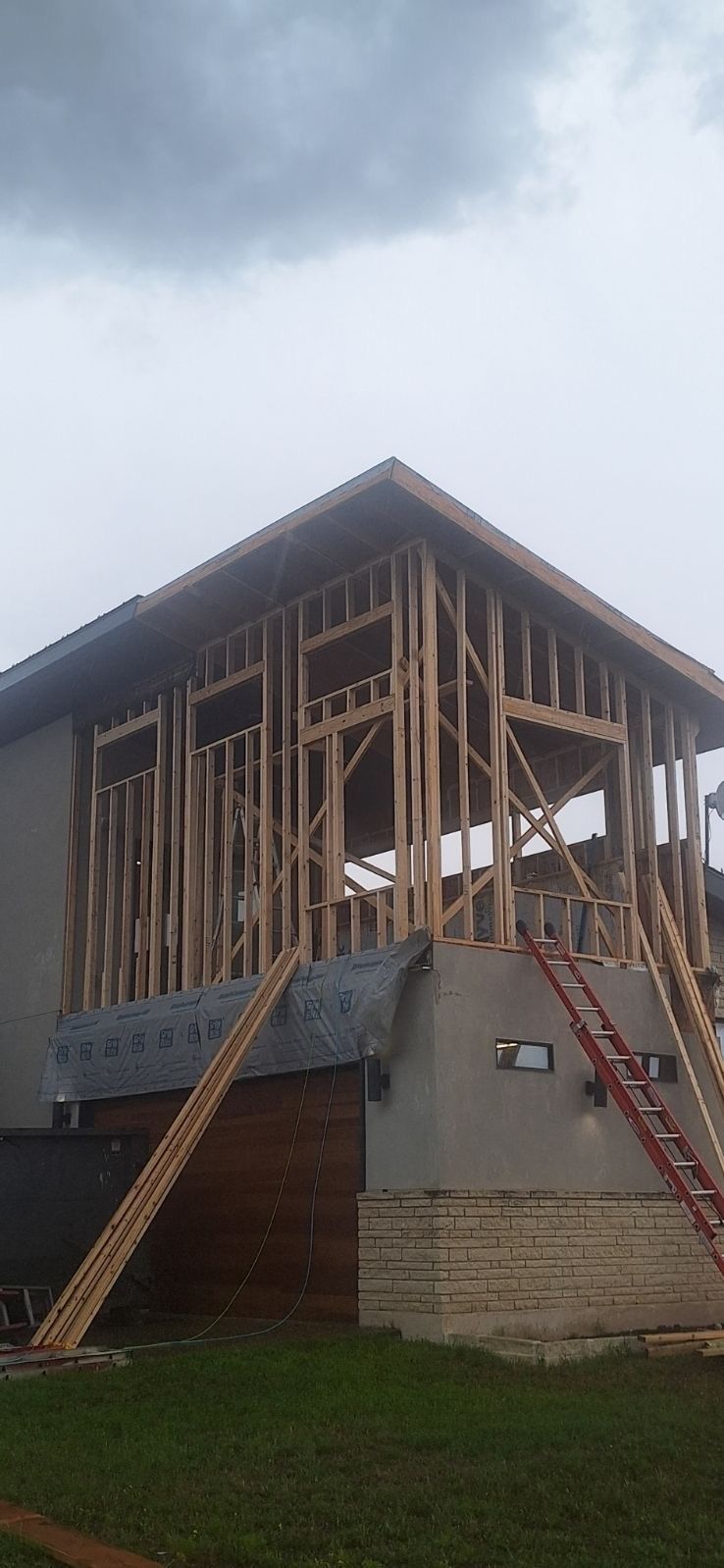 Wooden unfinished house frame with stairs and a concrete foundation on a grassy slope