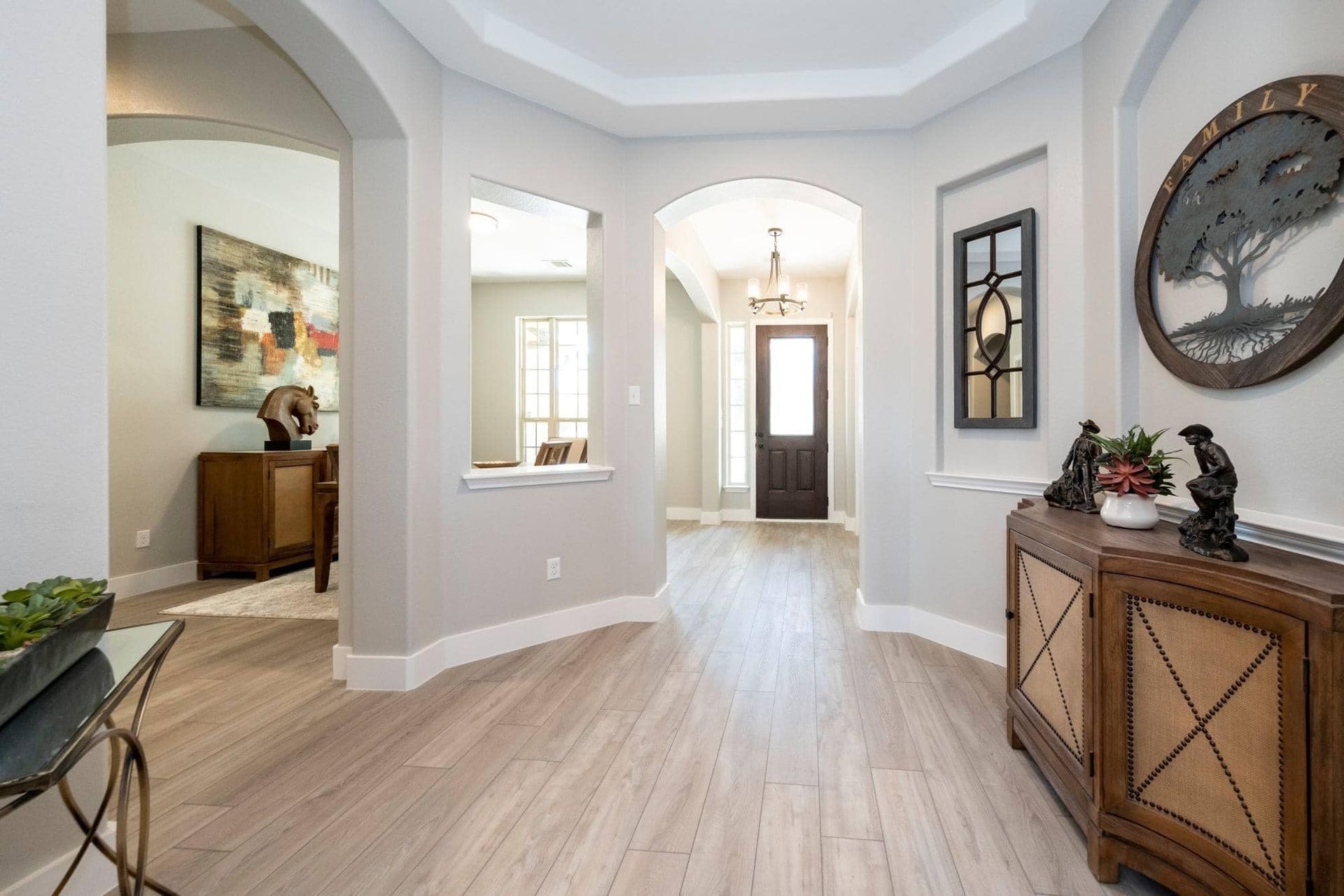Bright entry hallway with light wood floors, white walls, decorative console tables, and wall art.