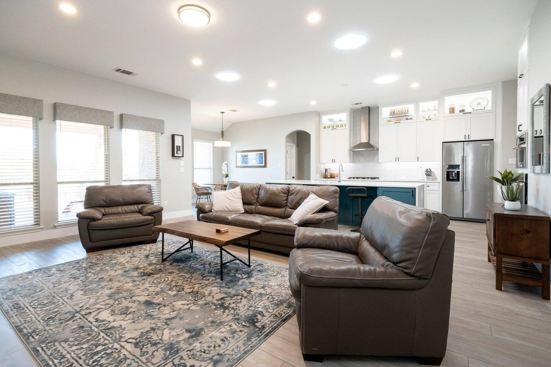 Bright living room with gray sofas, patterned rug, armchair, and open kitchen in the background
