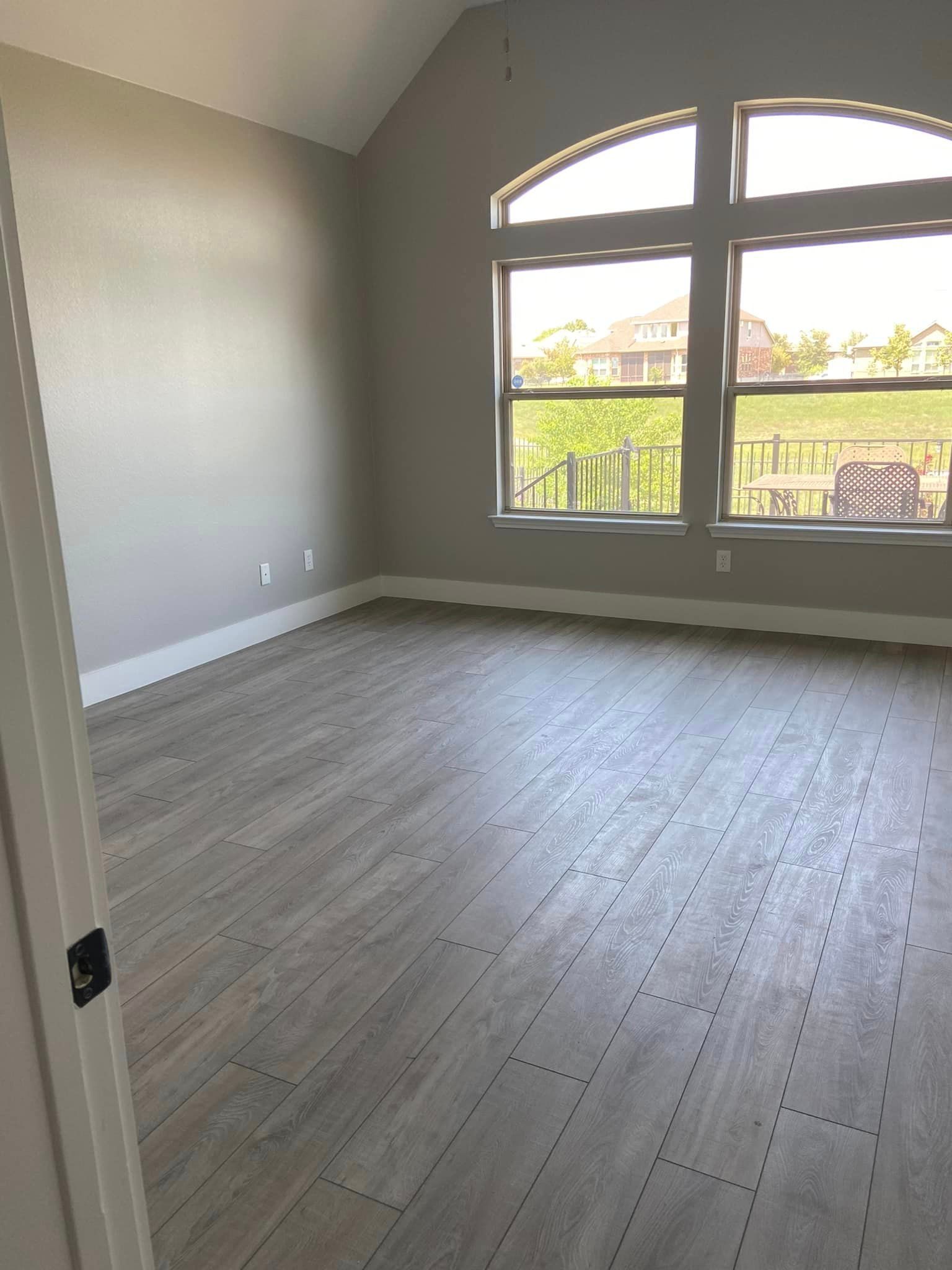 Empty room with gray wood floors, beige walls, and a large arched window letting in daylight