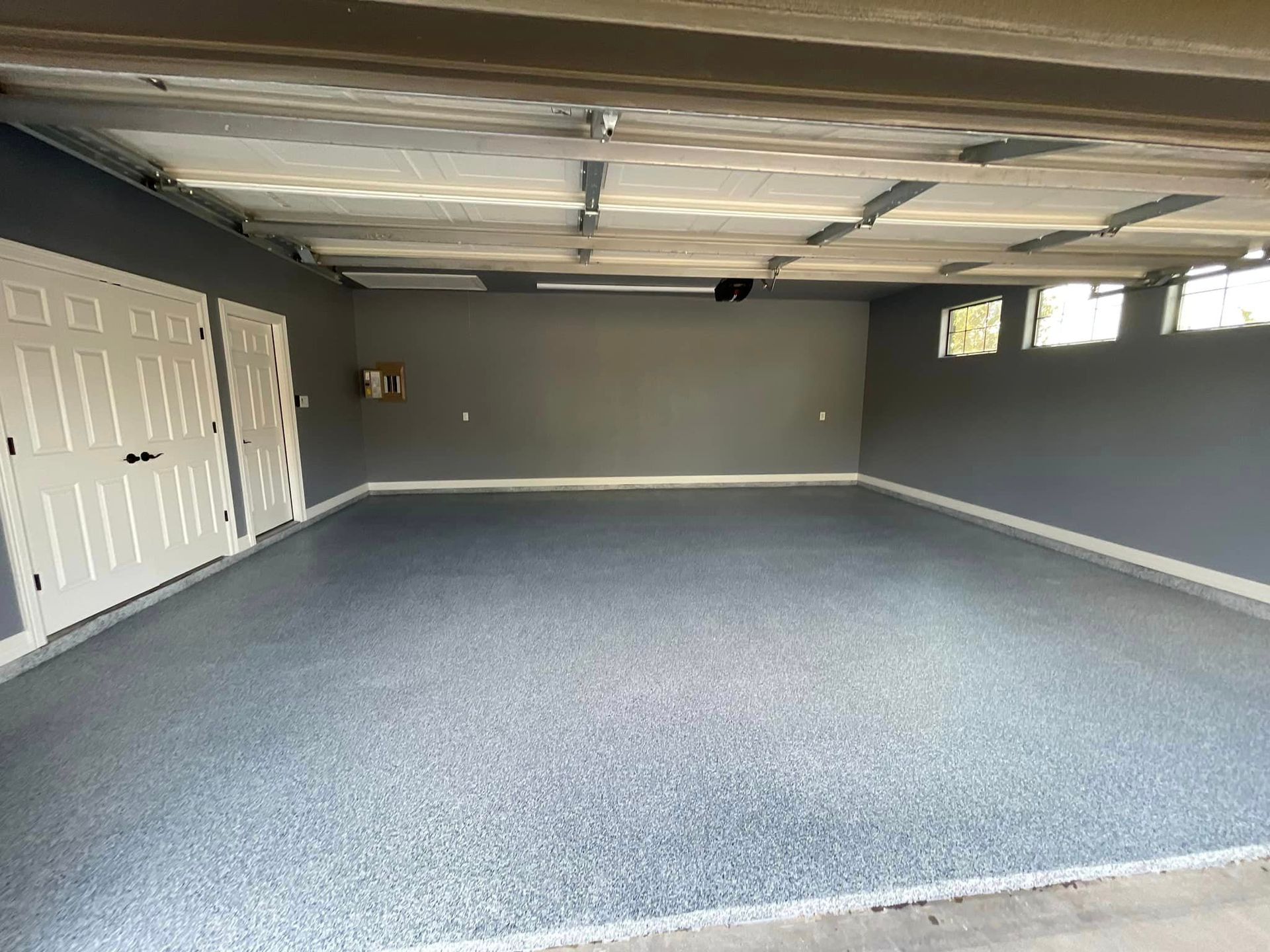 Empty garage interior with gray carpet, white garage doors, and gray walls