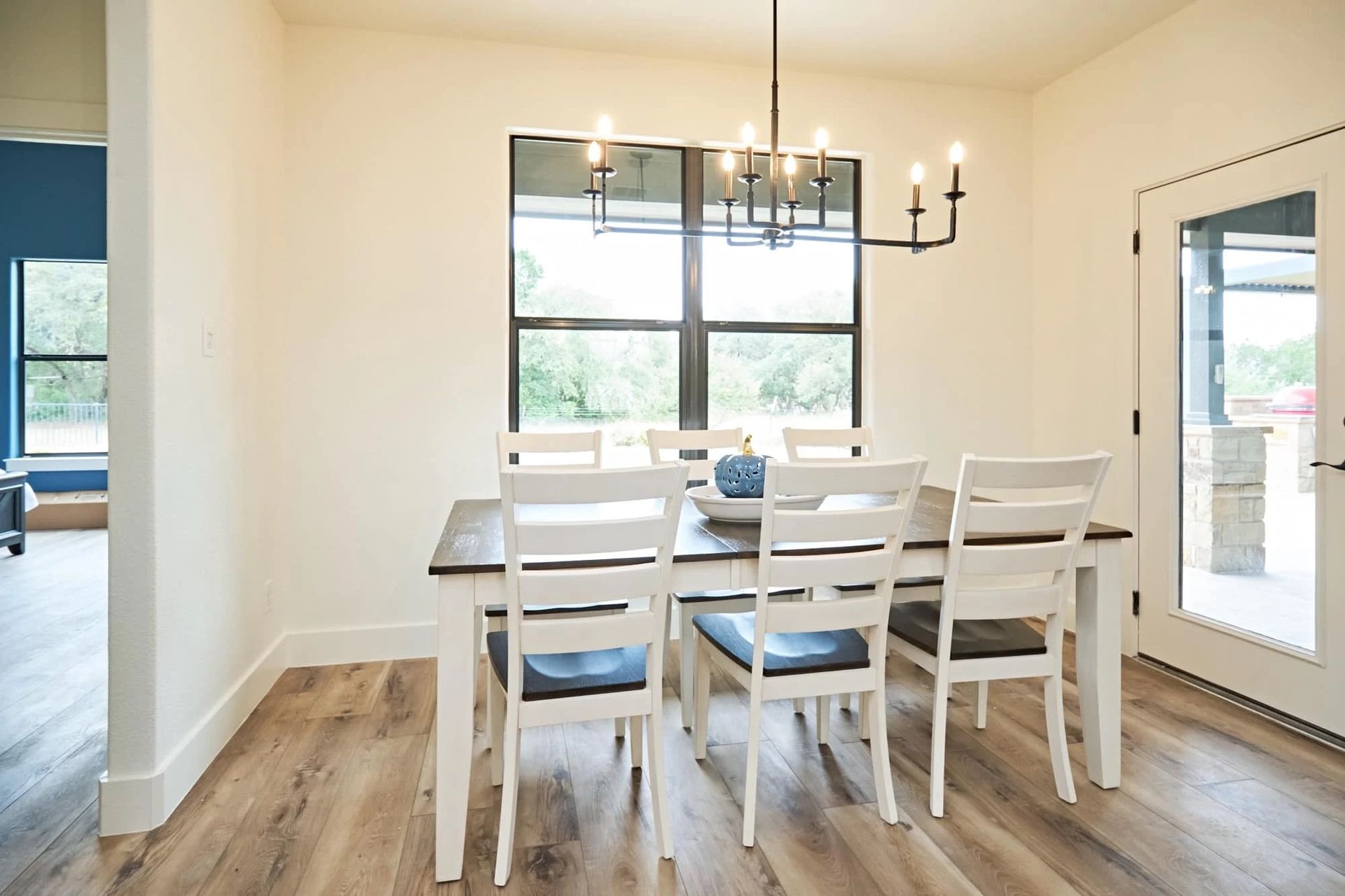 Bright dining room with white table, chairs, wood floors, large window, and chandelier