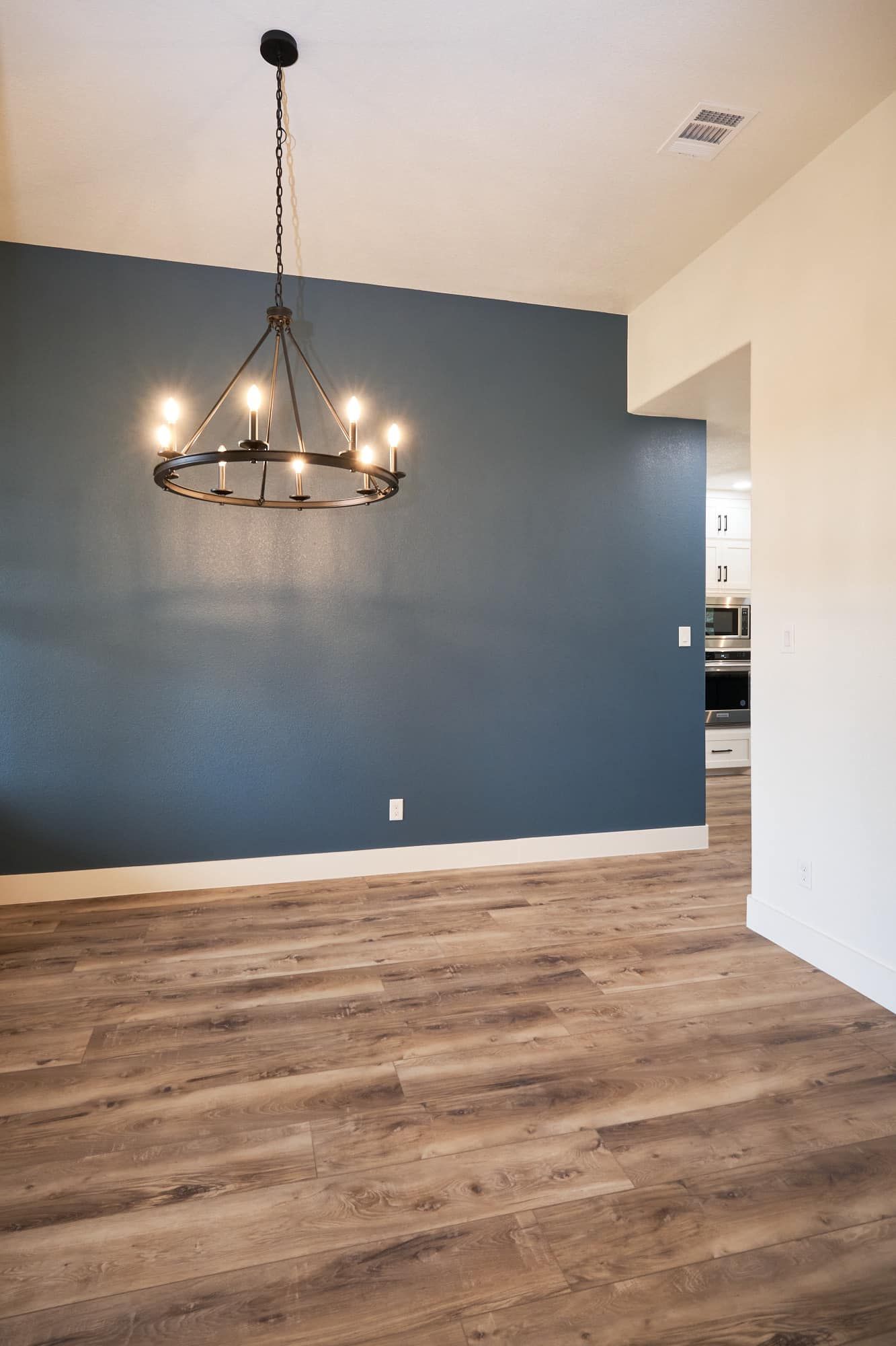 Empty dining room with blue accent wall, black chandelier, and wood-look flooring