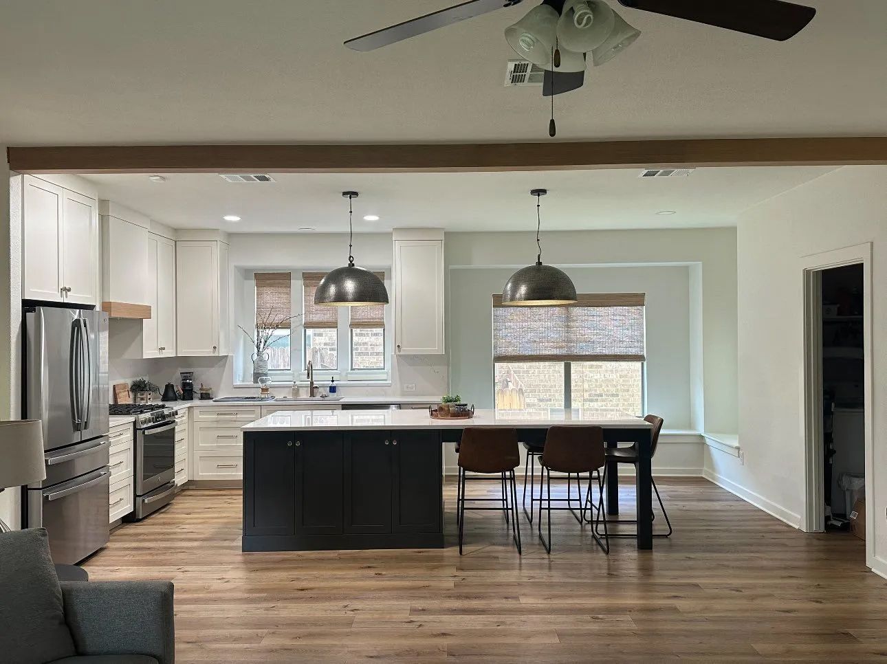 Bright open kitchen and dining area with white cabinets, dark island, wood floors, and pendant lights