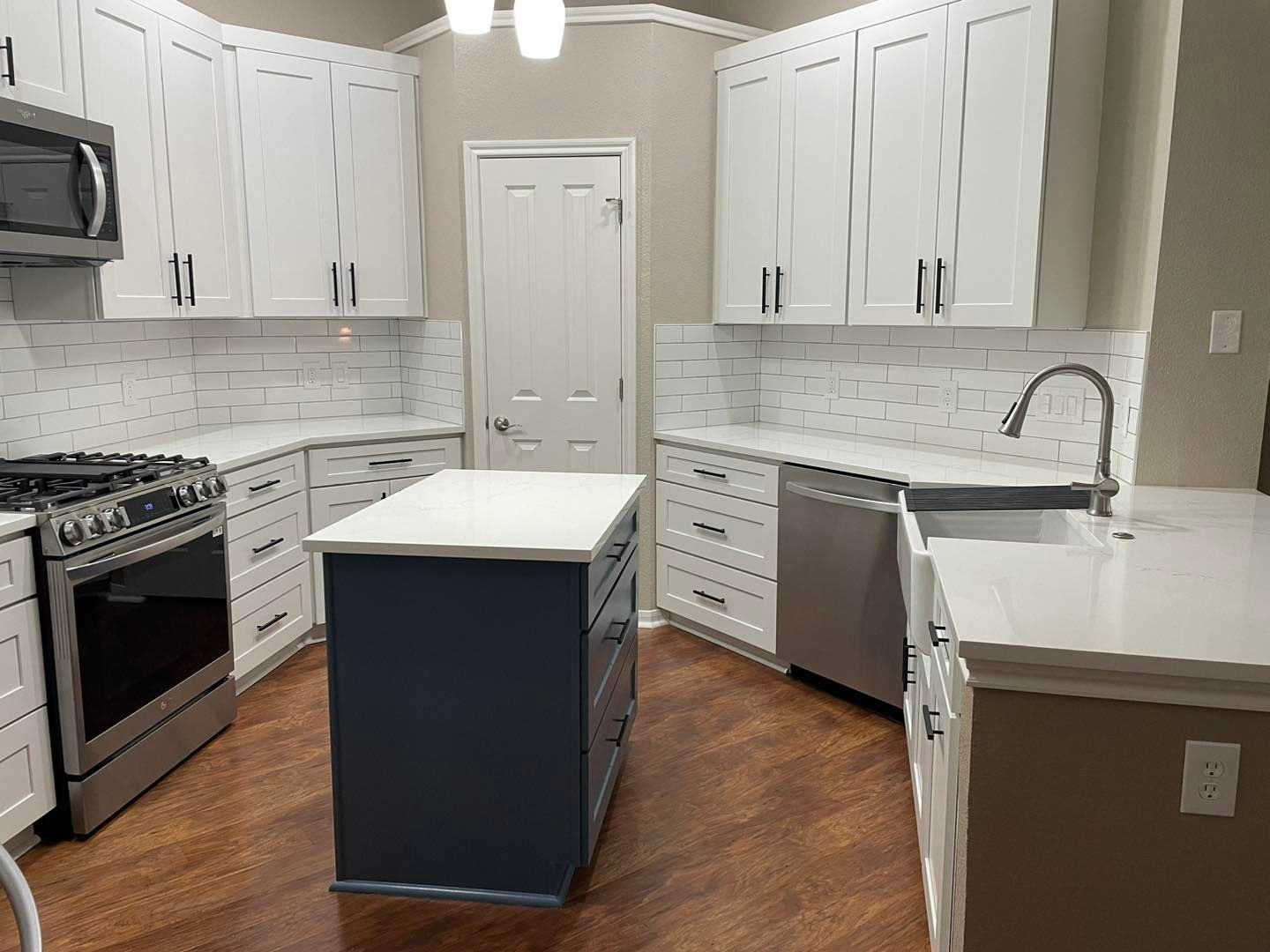 Modern kitchen with white cabinets, stainless appliances, wood floors, and a blue island in the center