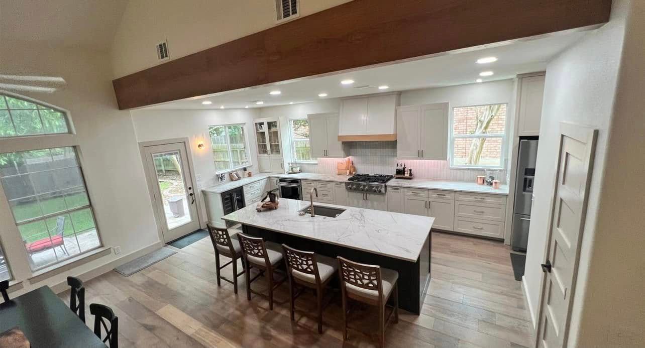 Spacious modern kitchen with a large island, white cabinets, wood floors, and exposed ceiling beam