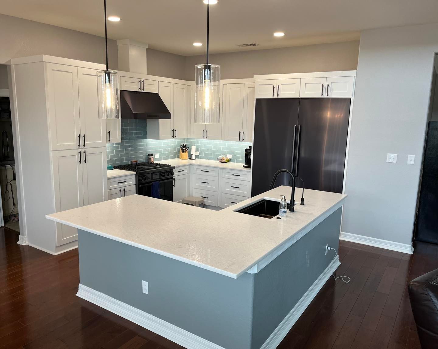 Bright modern kitchen with white cabinets, dark floors, and a large island with sink and pendant lights