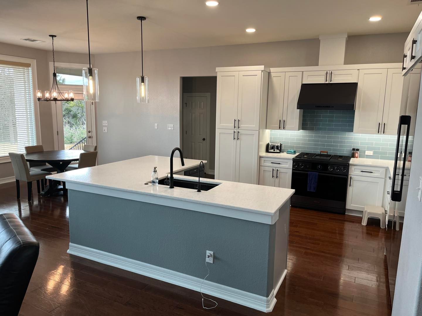 Modern kitchen with blue island, white cabinets, black fixtures, and hardwood floors