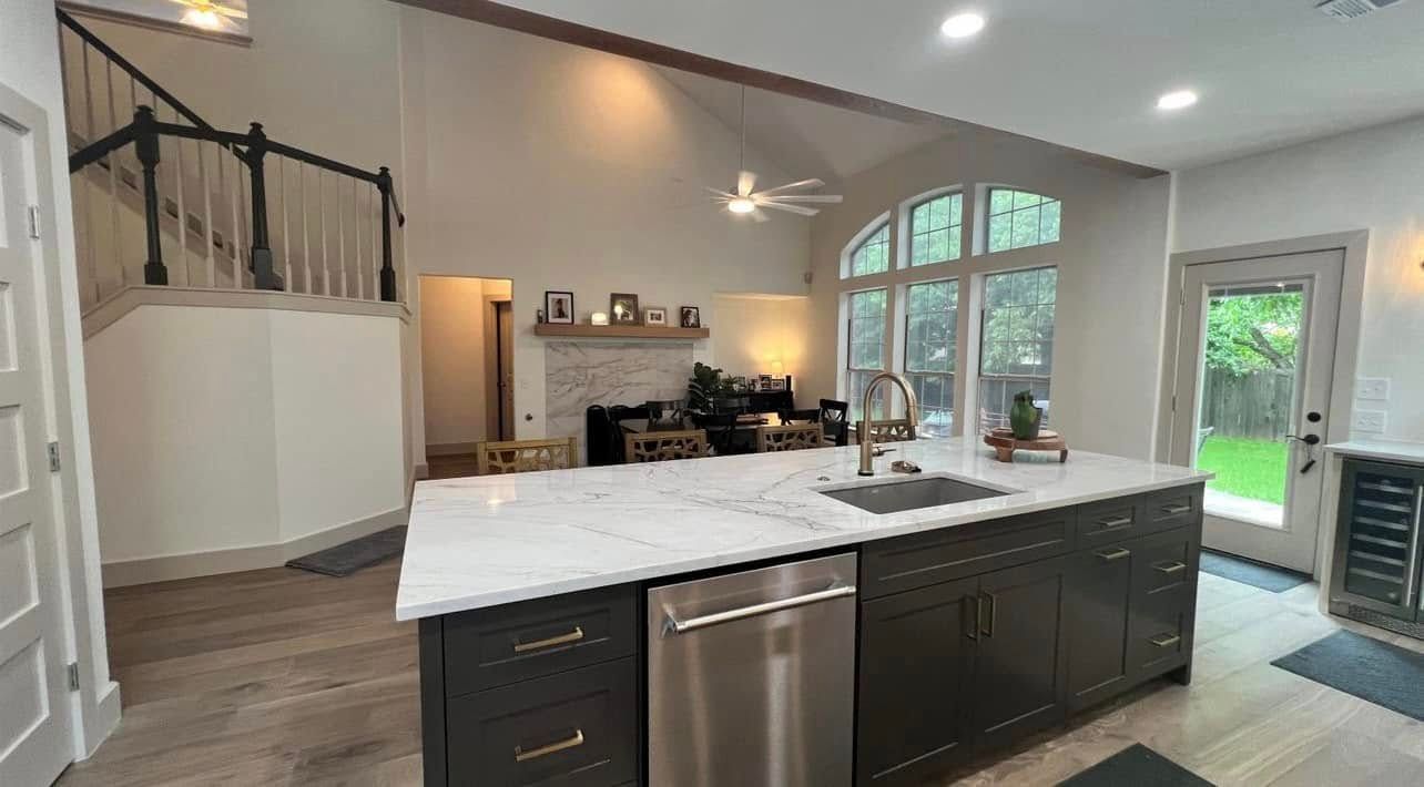 Bright modern kitchen with white island, dark cabinets, and large arched window leading to a patio.