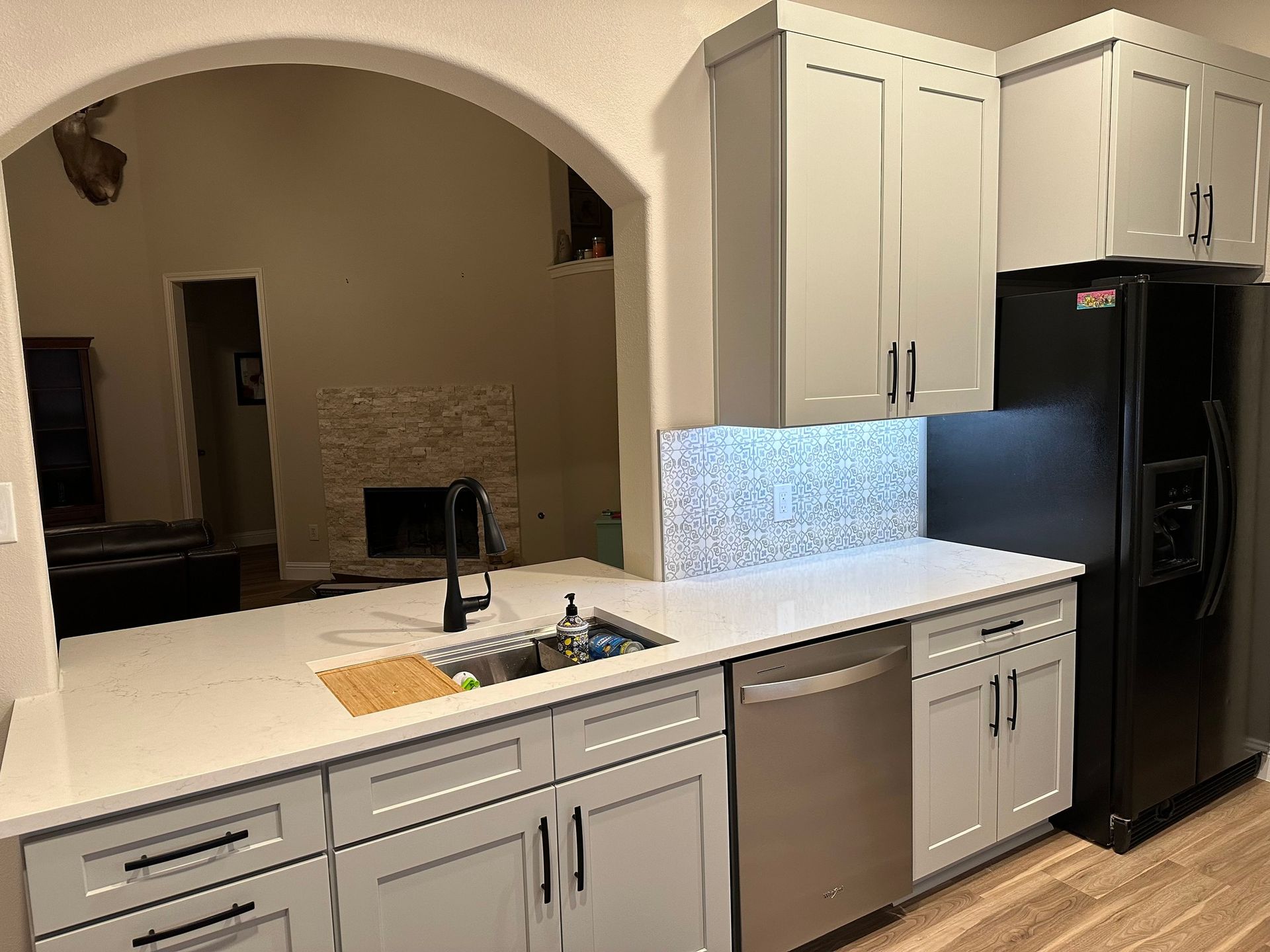 Modern kitchen with white cabinets, black refrigerator, stainless dishwasher, and white countertops under archway.