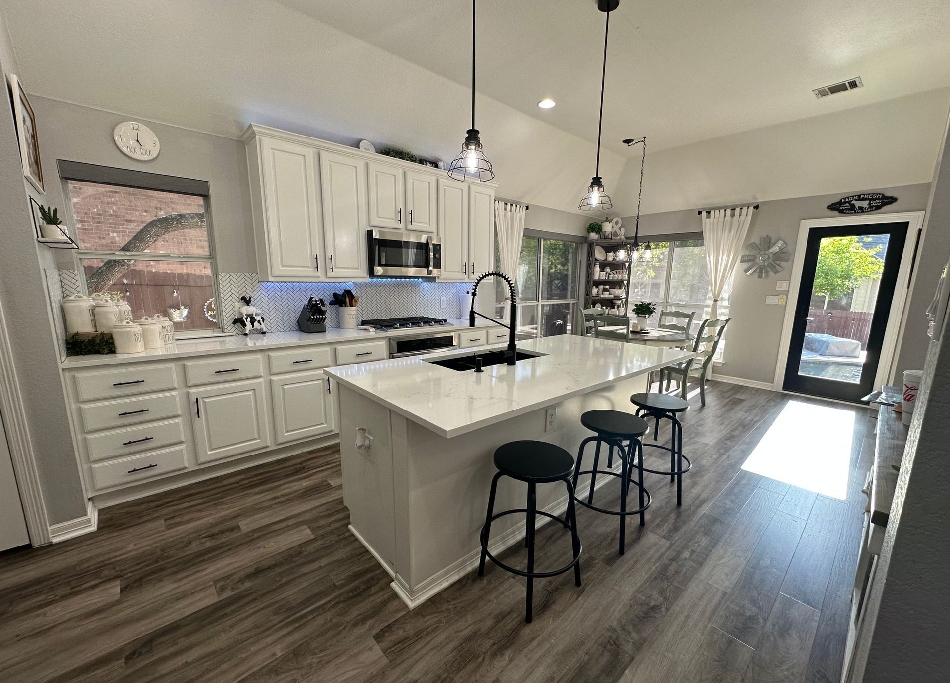 Bright modern kitchen with white cabinets, large island, black stools, and wood-look flooring