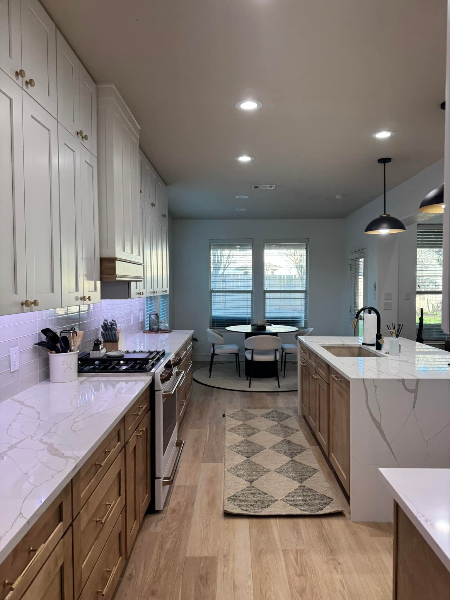 Bright modern kitchen with white cabinets, island, pendant light, and dining area by windows