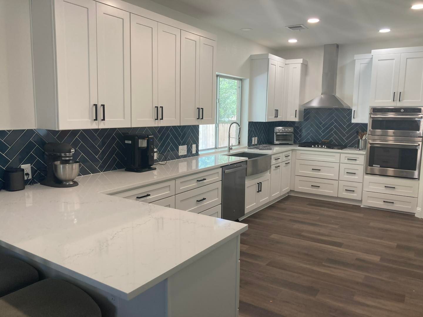 Modern white kitchen with dark backsplash, stainless appliances, and wood flooring