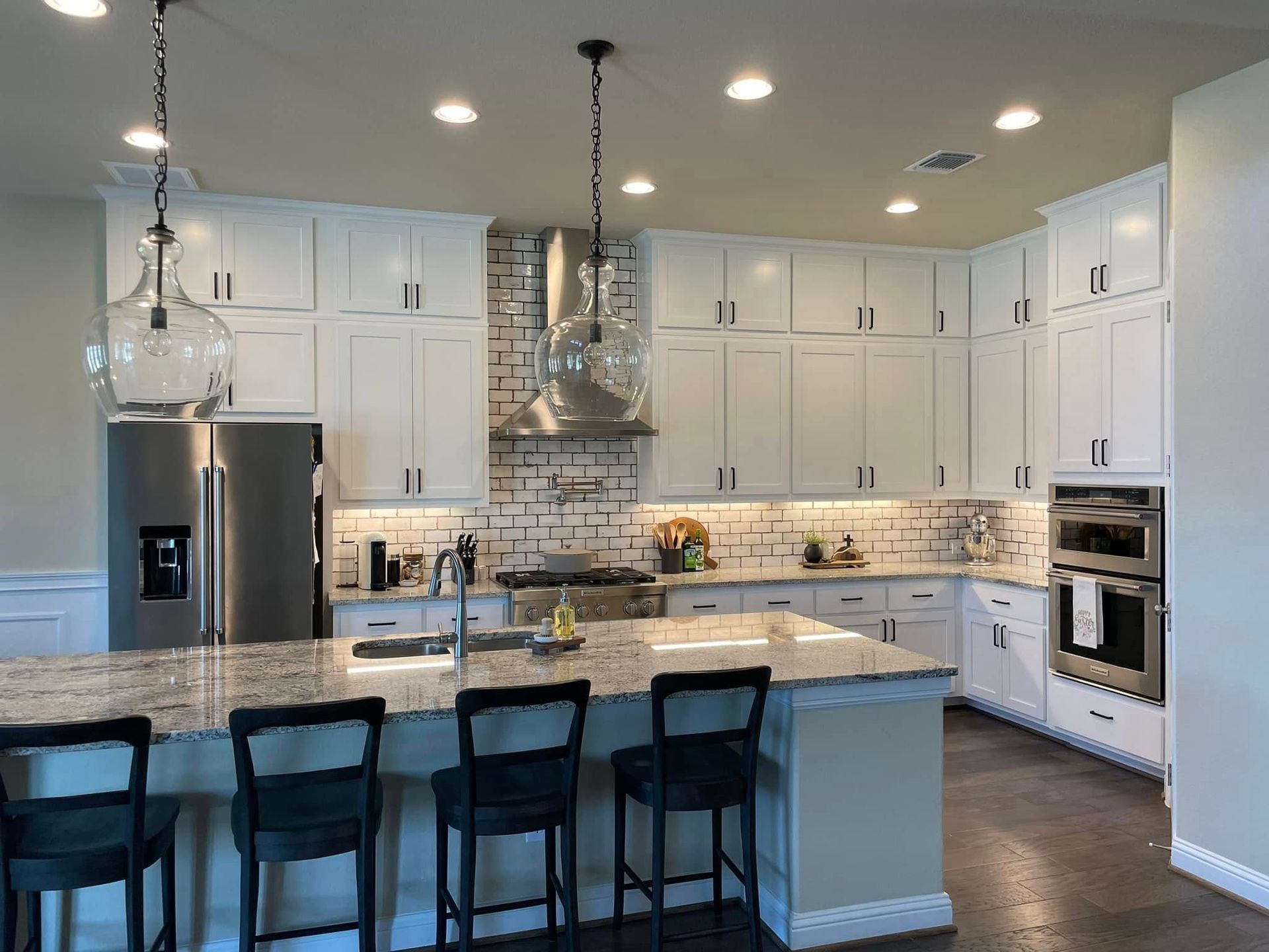 Bright modern kitchen with white cabinets, granite island, stainless appliances, and four black stools