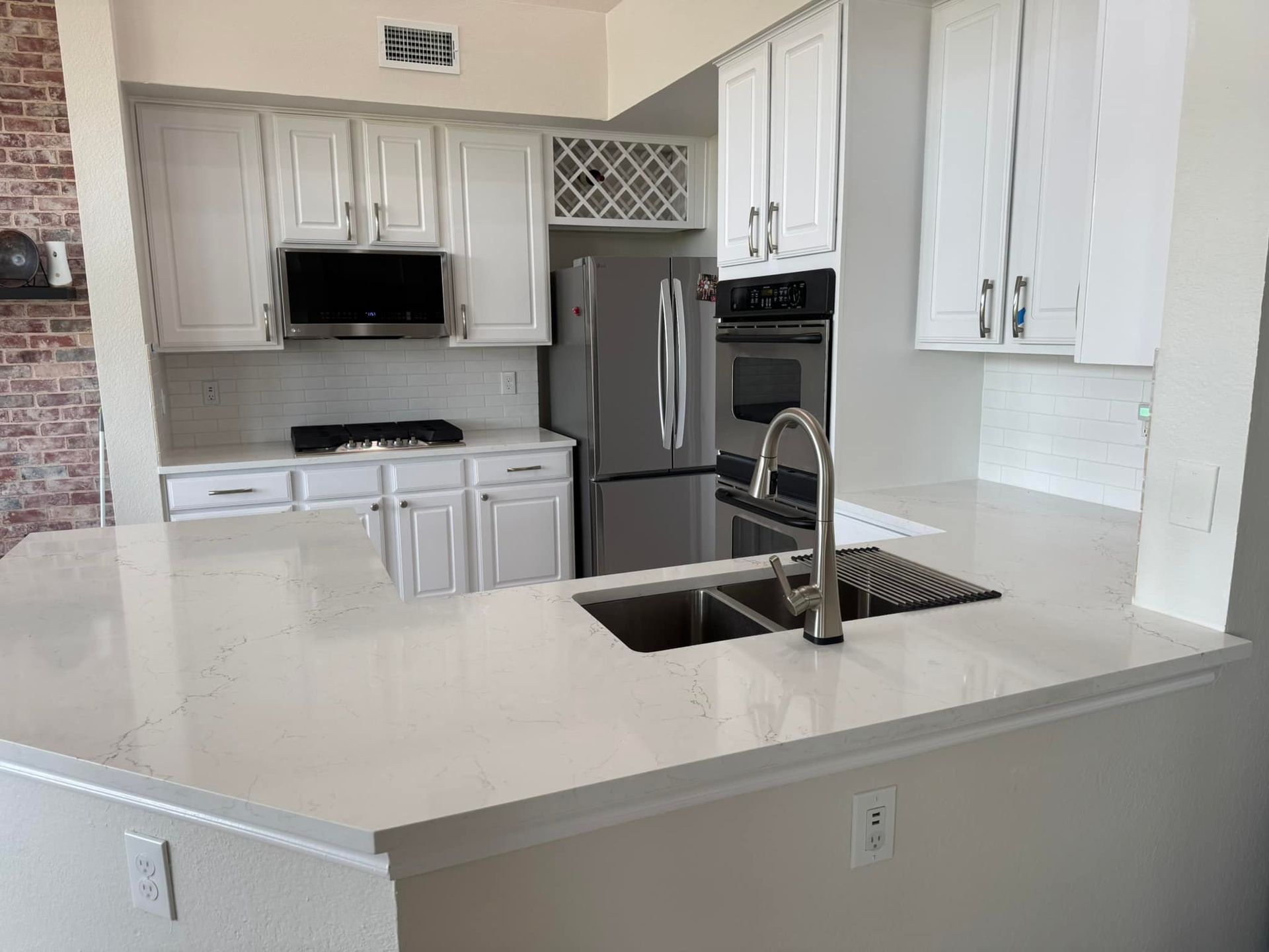 Bright modern kitchen with white cabinets, stainless appliances, and a large quartz island with sink and faucet