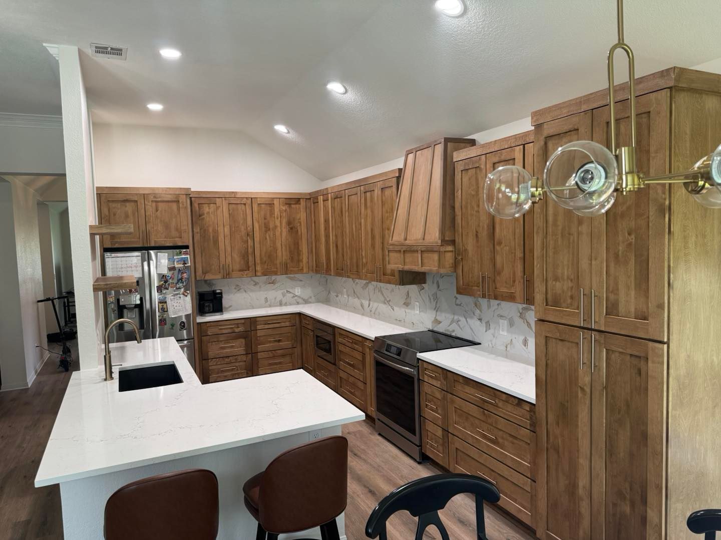 Modern kitchen with wood cabinets, white counters, marble backsplash, and a peninsula with barstools and pendant lights