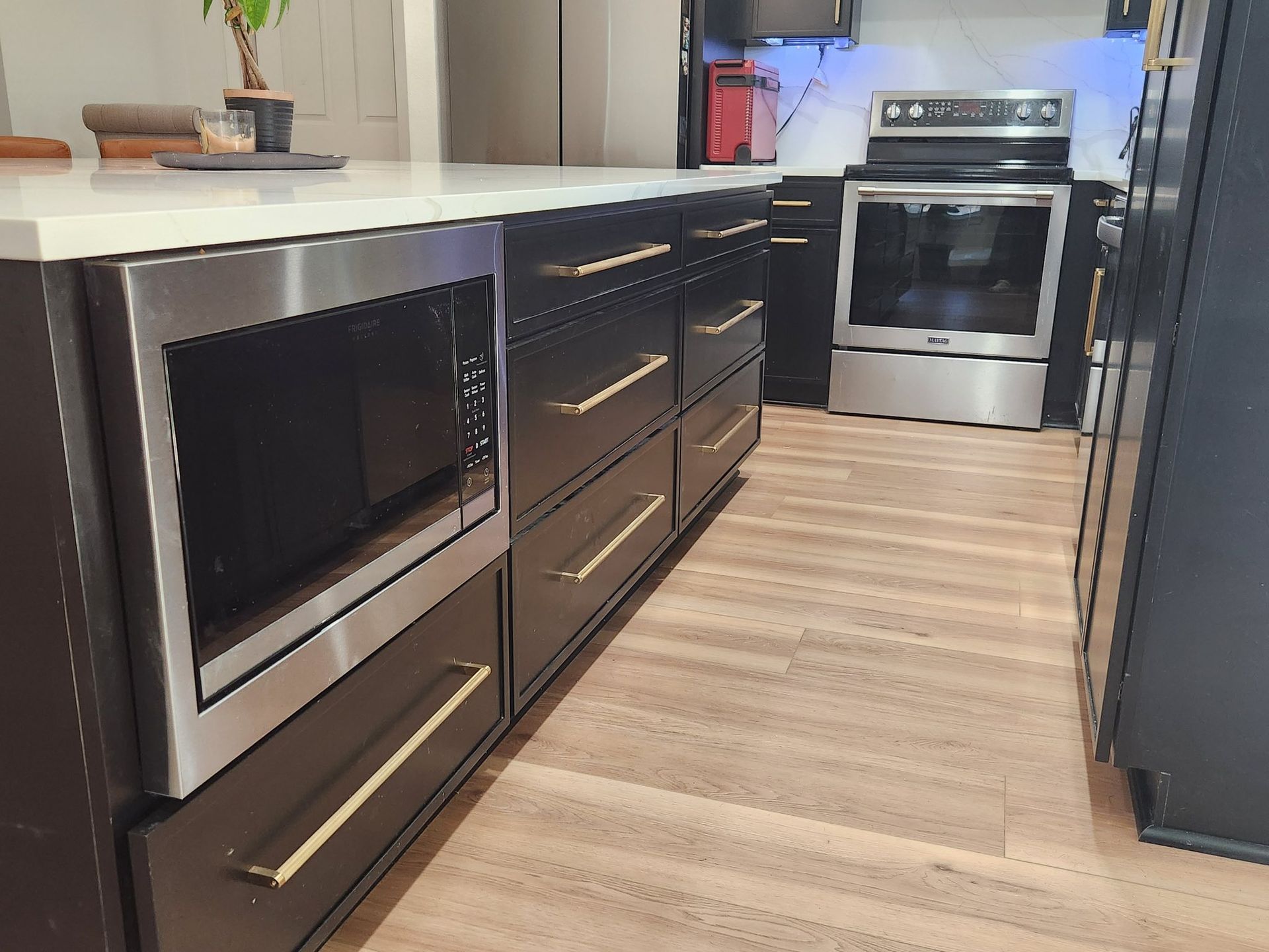 Modern kitchen with dark cabinets, stainless steel appliances, and light wood flooring.