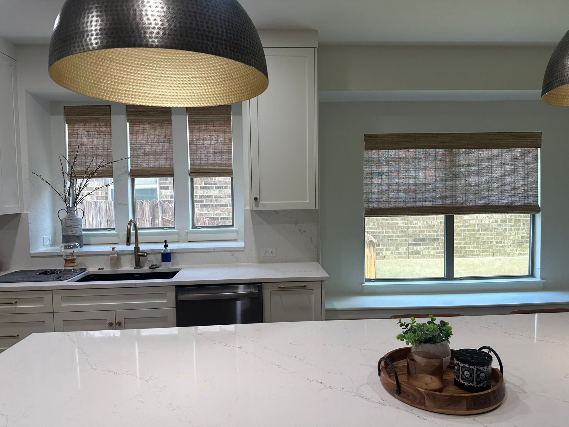 Bright modern kitchen with white cabinets, large pendants, and a window over the sink.