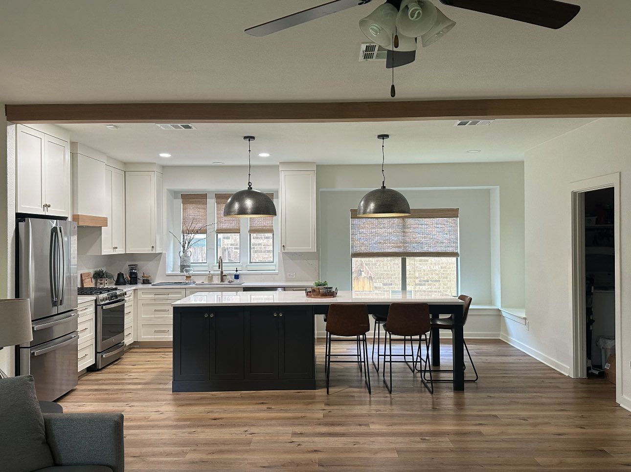 Open-concept kitchen and dining area with white cabinets, black island, wood floors, and pendant lights