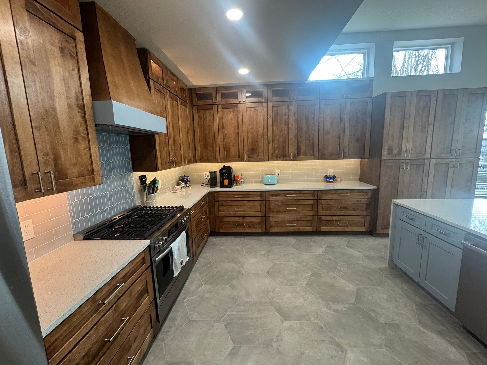 Empty rustic kitchen with wood cabinets, stainless stove, and large gray island under skylights.