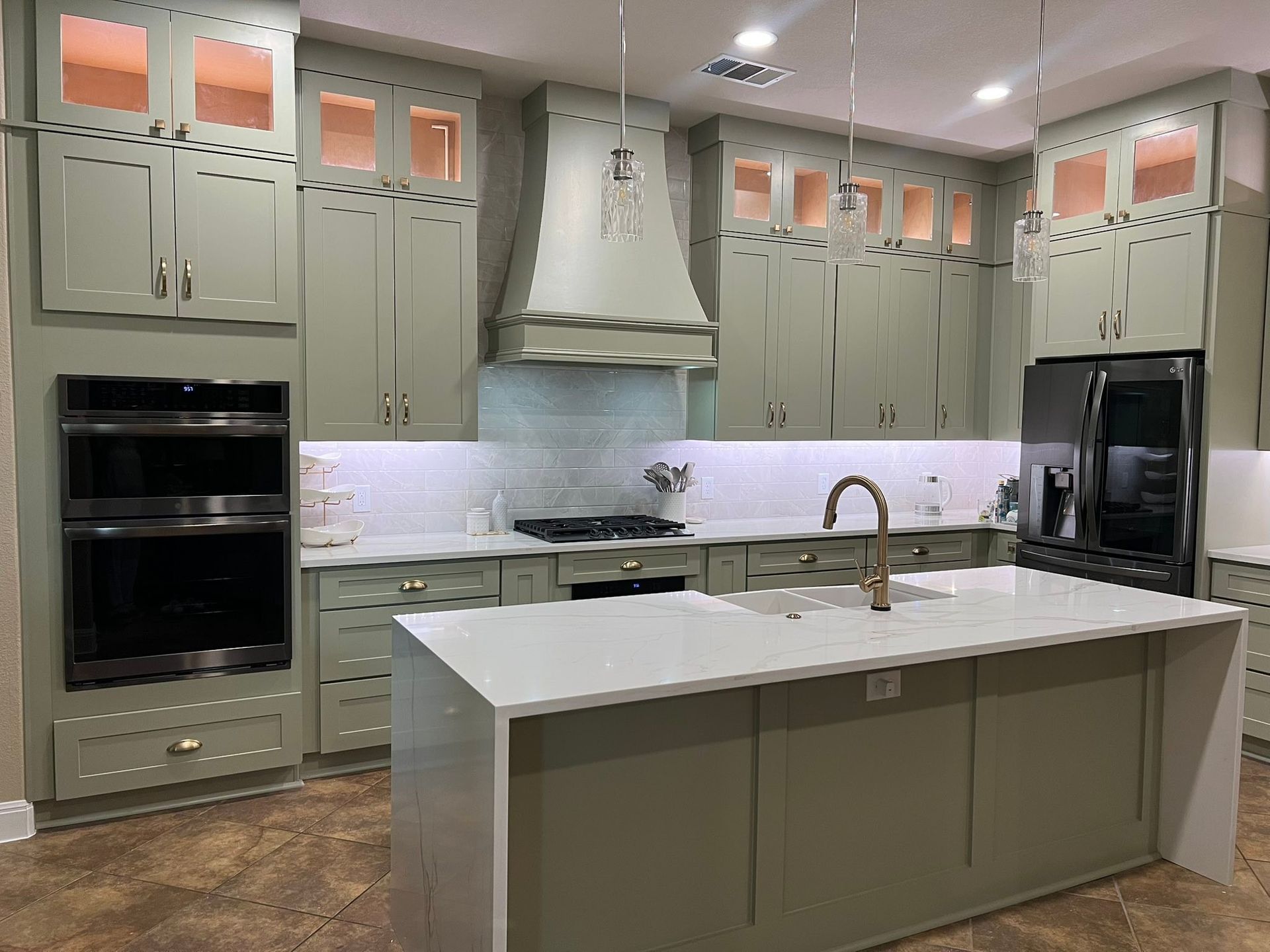 Modern kitchen with sage cabinets, white island, stainless appliances, and glass-front upper cabinets