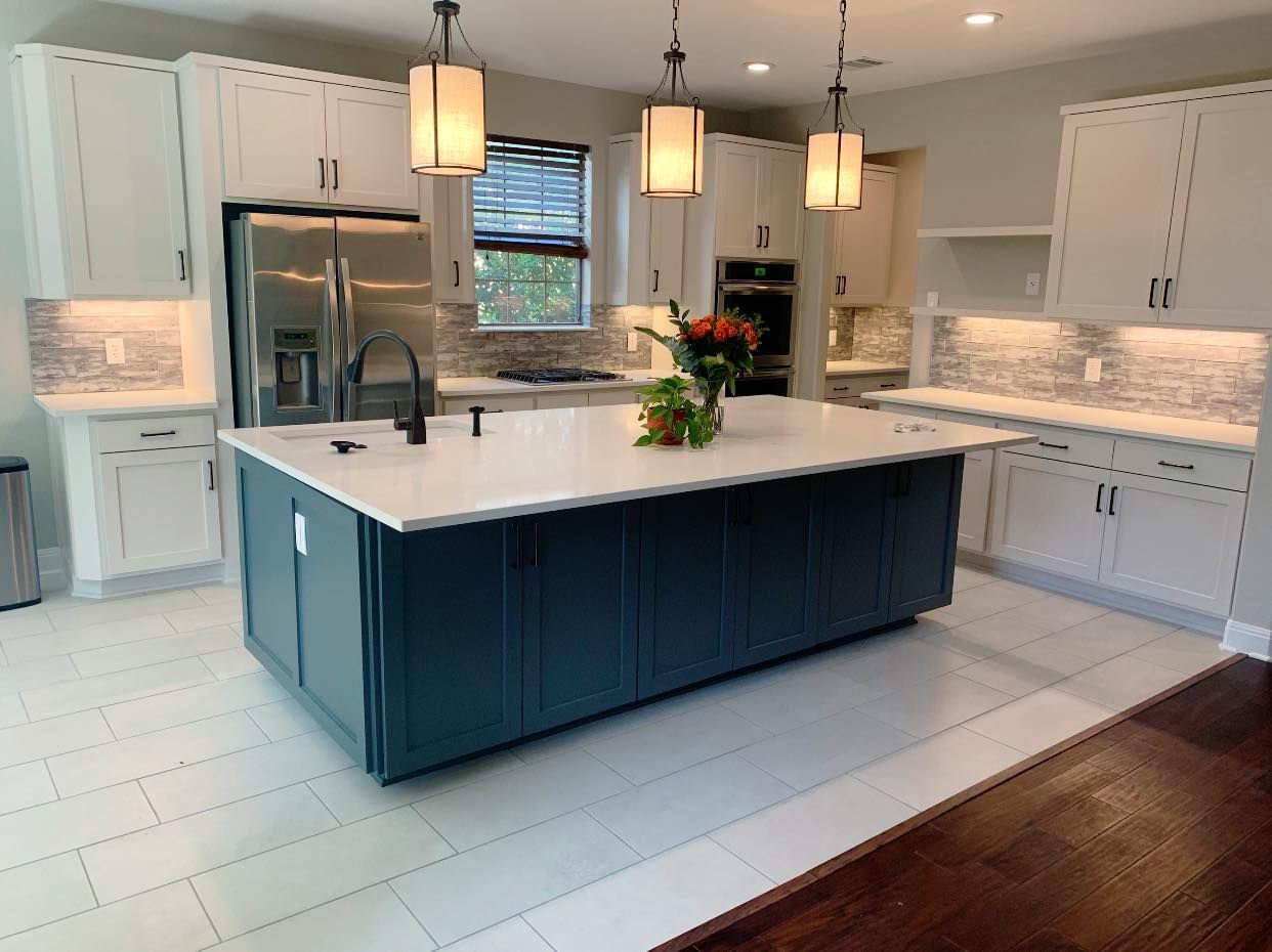 Modern white kitchen with blue island, pendant lights, marble counters, and dark wood floor