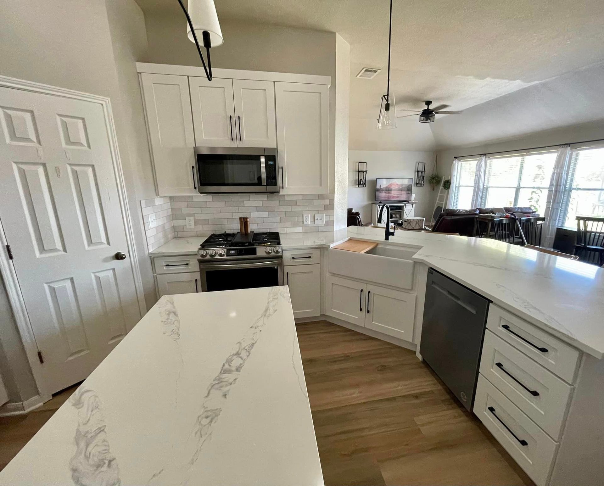 Bright modern kitchen with white cabinets, marble island, black appliances, and large windows