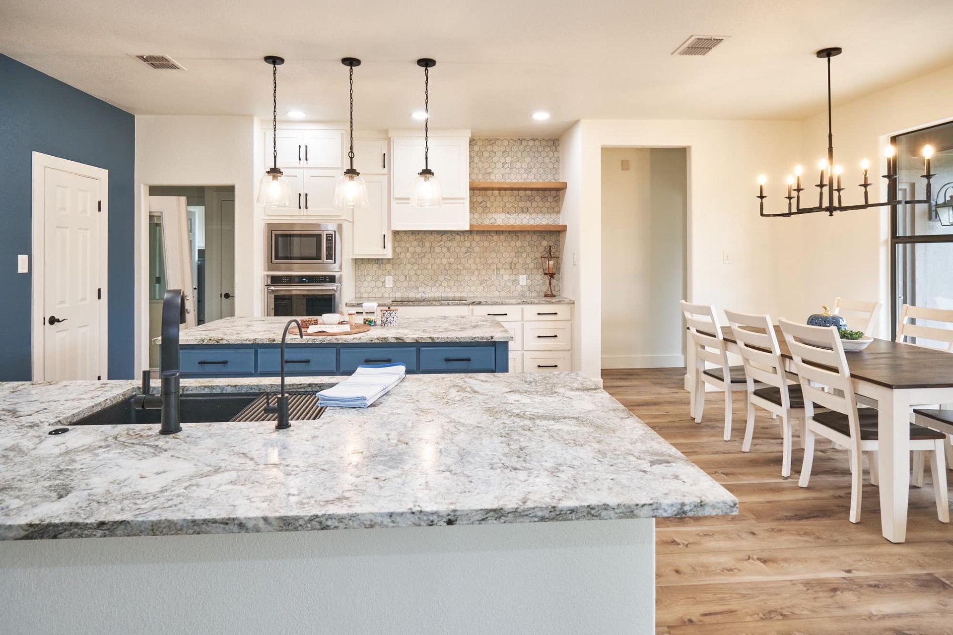 Bright modern kitchen and dining area with large island, white cabinets, pendant lights, and wood floors