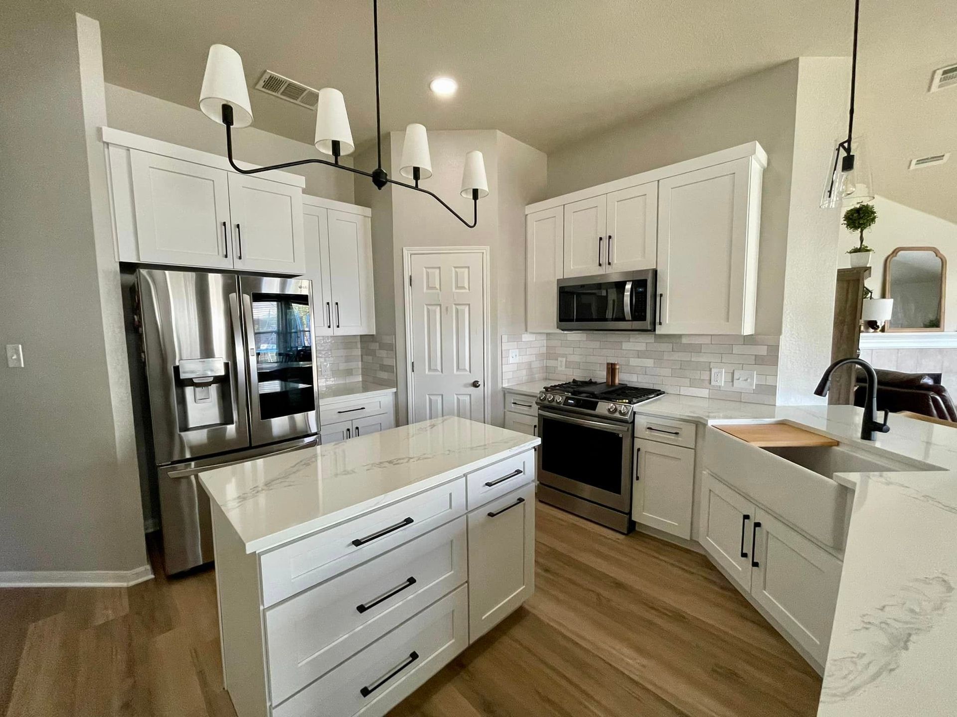 Bright modern kitchen with white cabinets, stainless appliances, island, and wood floors