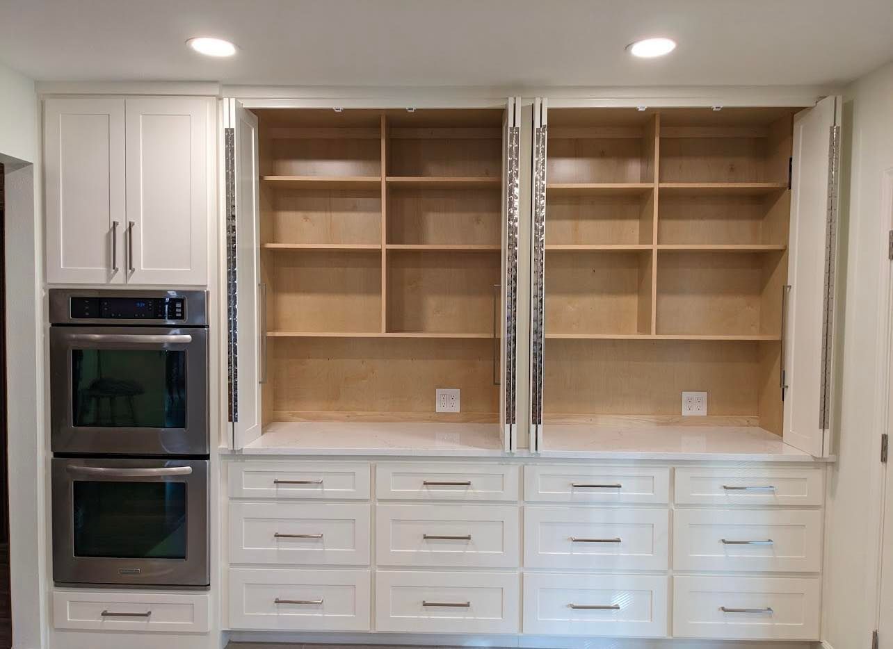 Built-in kitchen cabinetry with open shelves, white drawers, and a double wall oven on the left