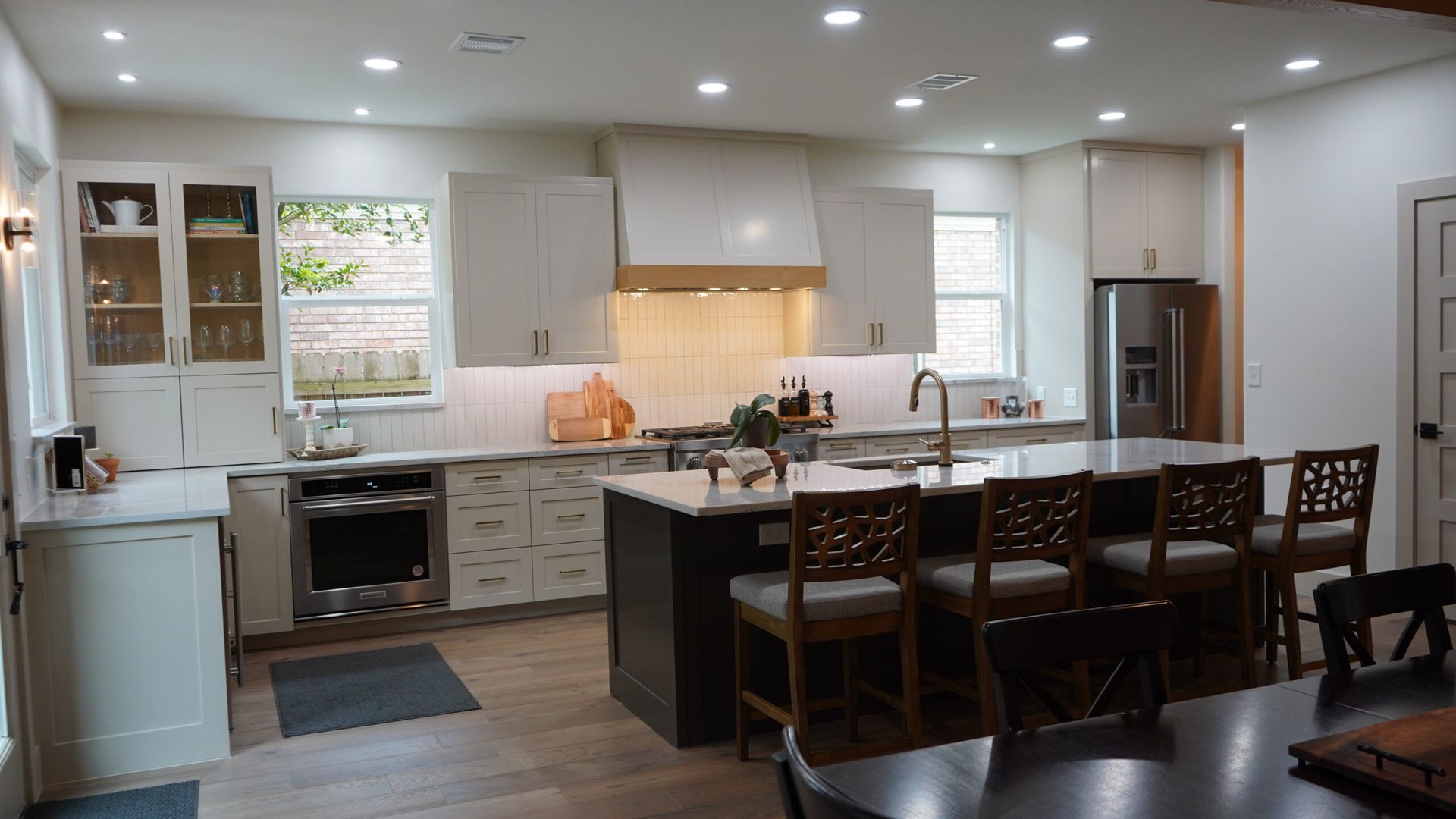 Modern white kitchen with island, bar stools, pendant lights, and dark wood dining table