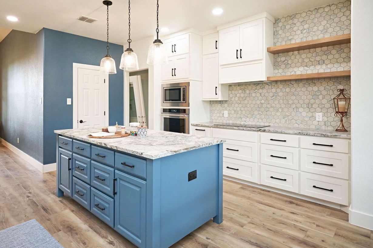 Bright modern kitchen with white cabinets, blue island, marble counters, and wood floors