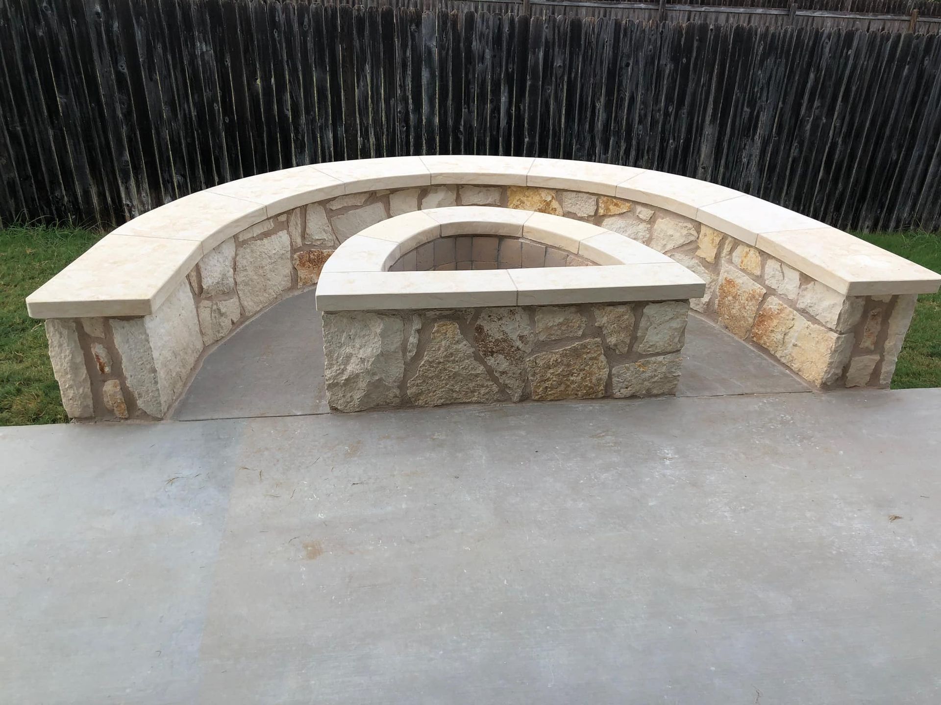 Stone benches with curved white tops in an outdoor paved area against a dark fence