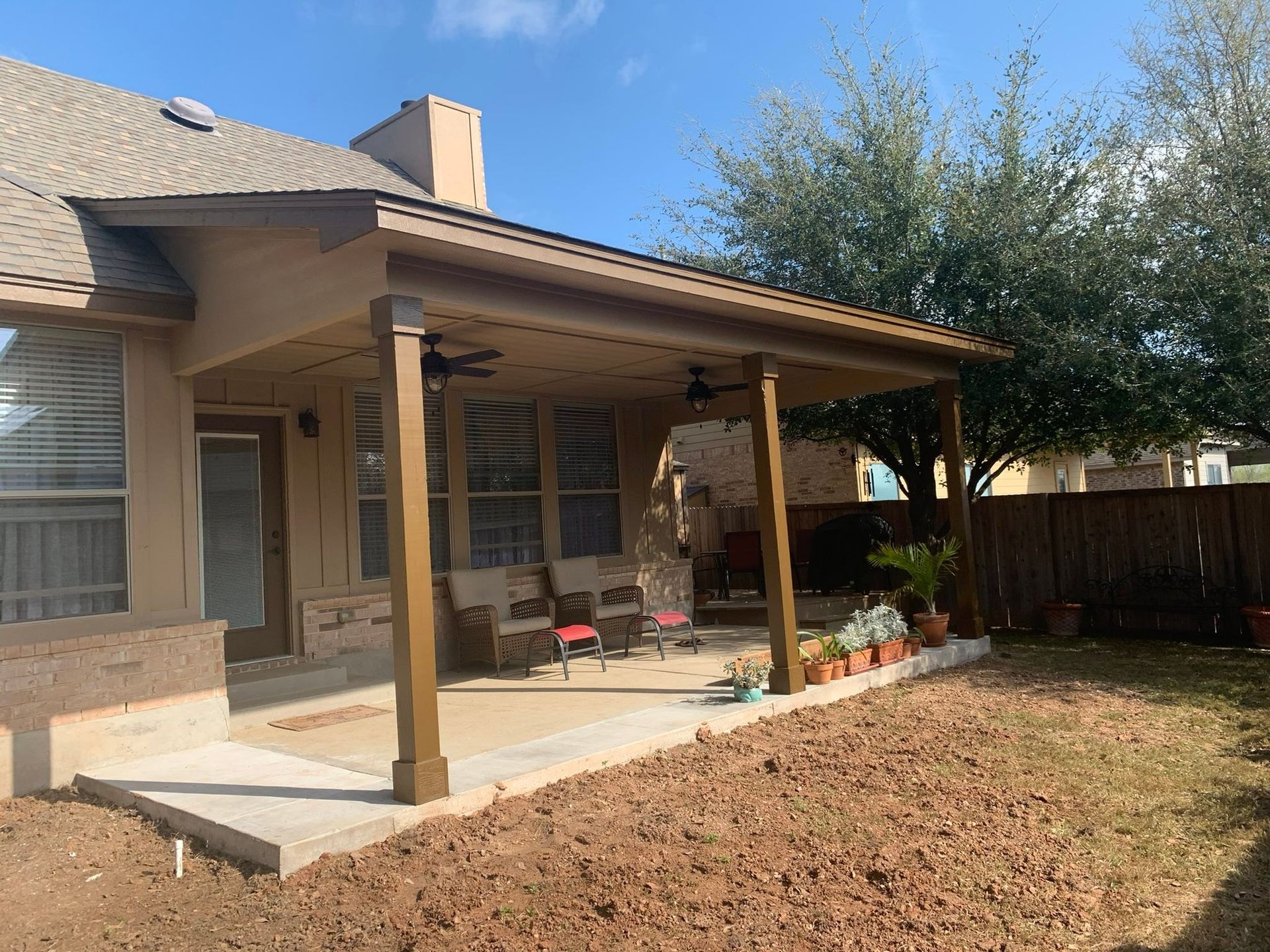 Backyard patio with a covered pergola, brick house, wooden posts, and dry yard lawn.