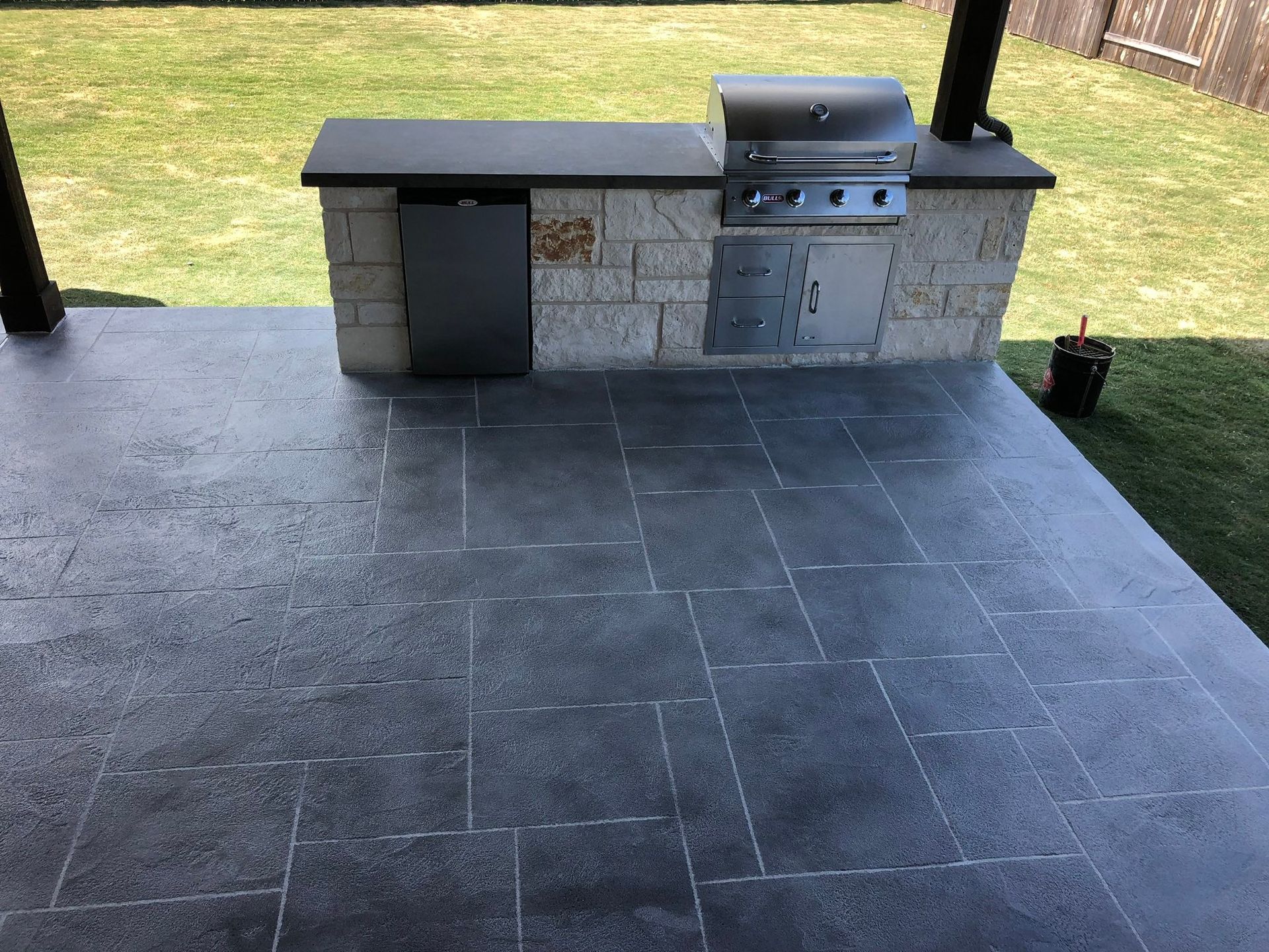 Outdoor patio with a built-in stone grill and counter beside a grassy yard
