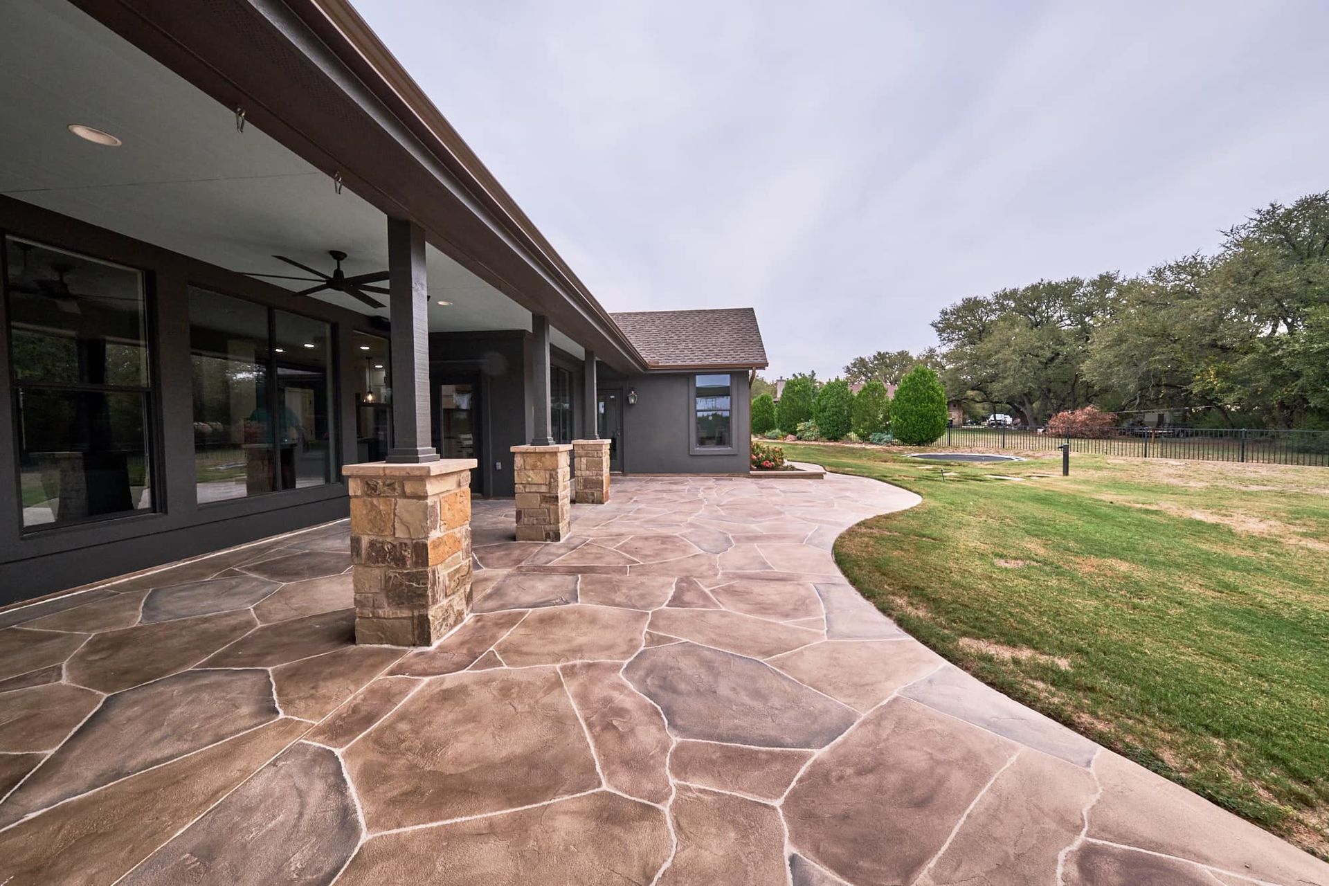 Stone patio beside a modern house, with covered porch columns and a grassy yard beyond.
