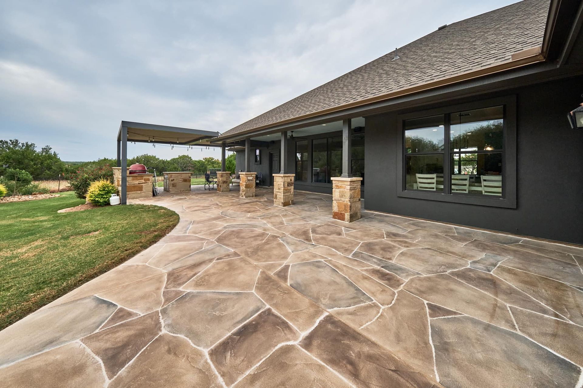 Stone patio beside a dark house with covered porch and grassy yard under a cloudy sky