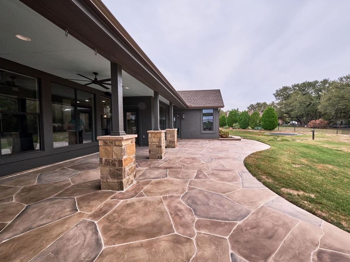 Stone patio walkway beside a modern building with columns, glass windows, and a curved grassy lawn.