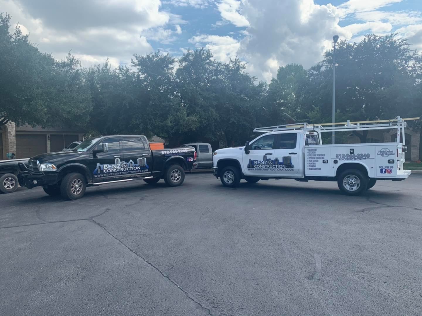 Two work trucks with utility trailers parked in a lot under cloudy skies