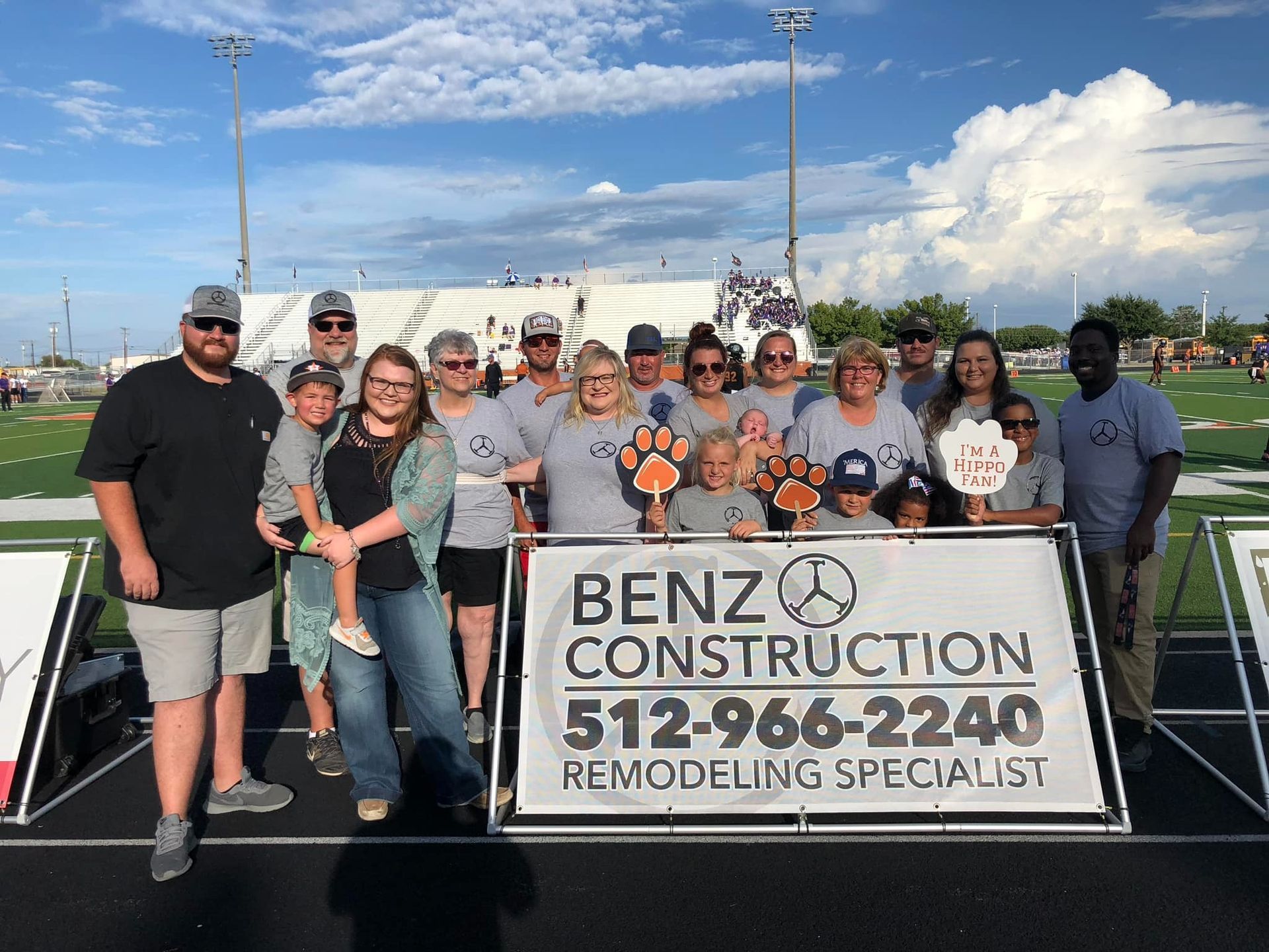 Group posing outdoors behind a Benz Construction remodeling specialist sign on a sunny day.